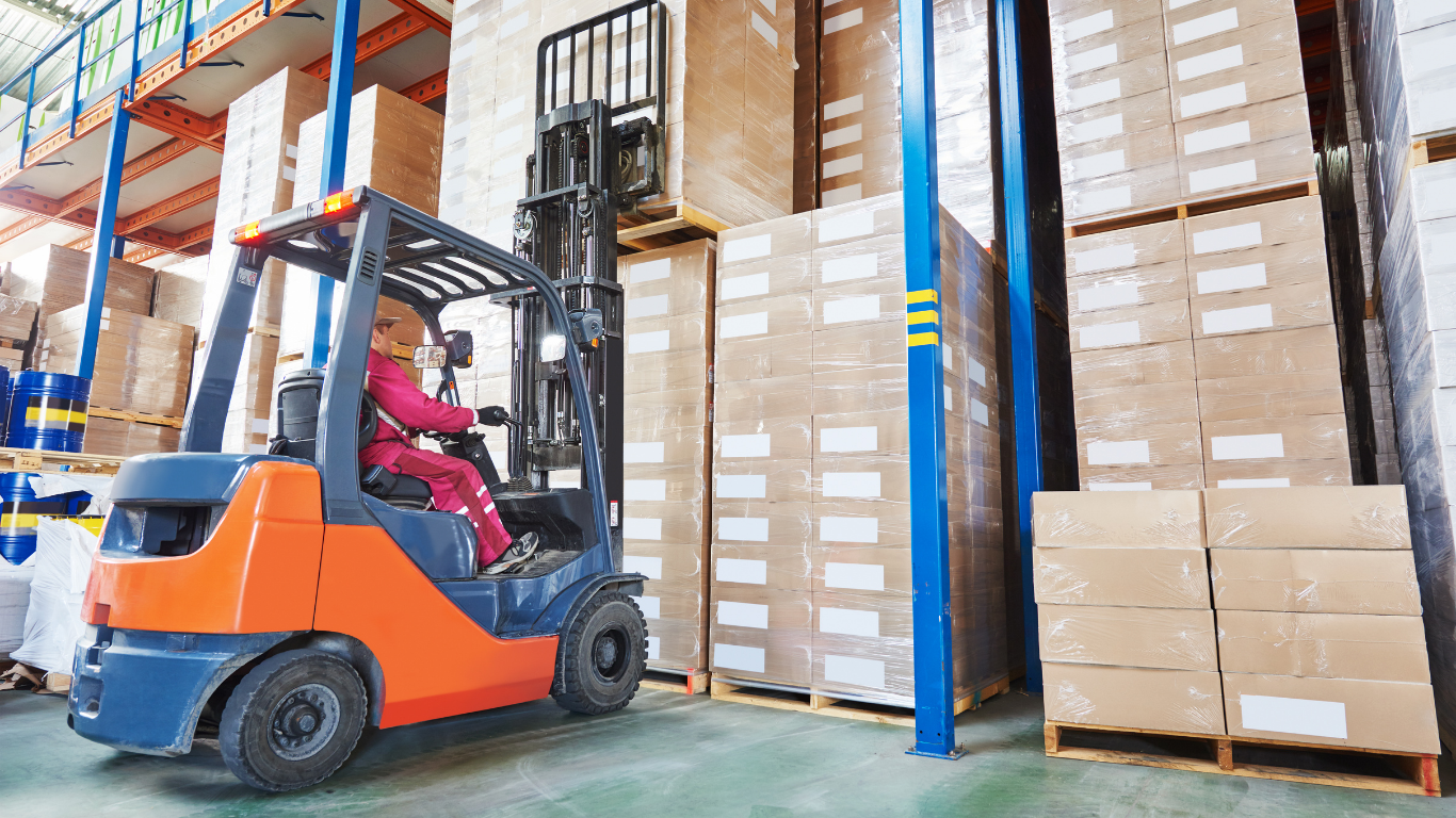Forklift in a warehouse moving stacked cardboard boxes on tall shelves