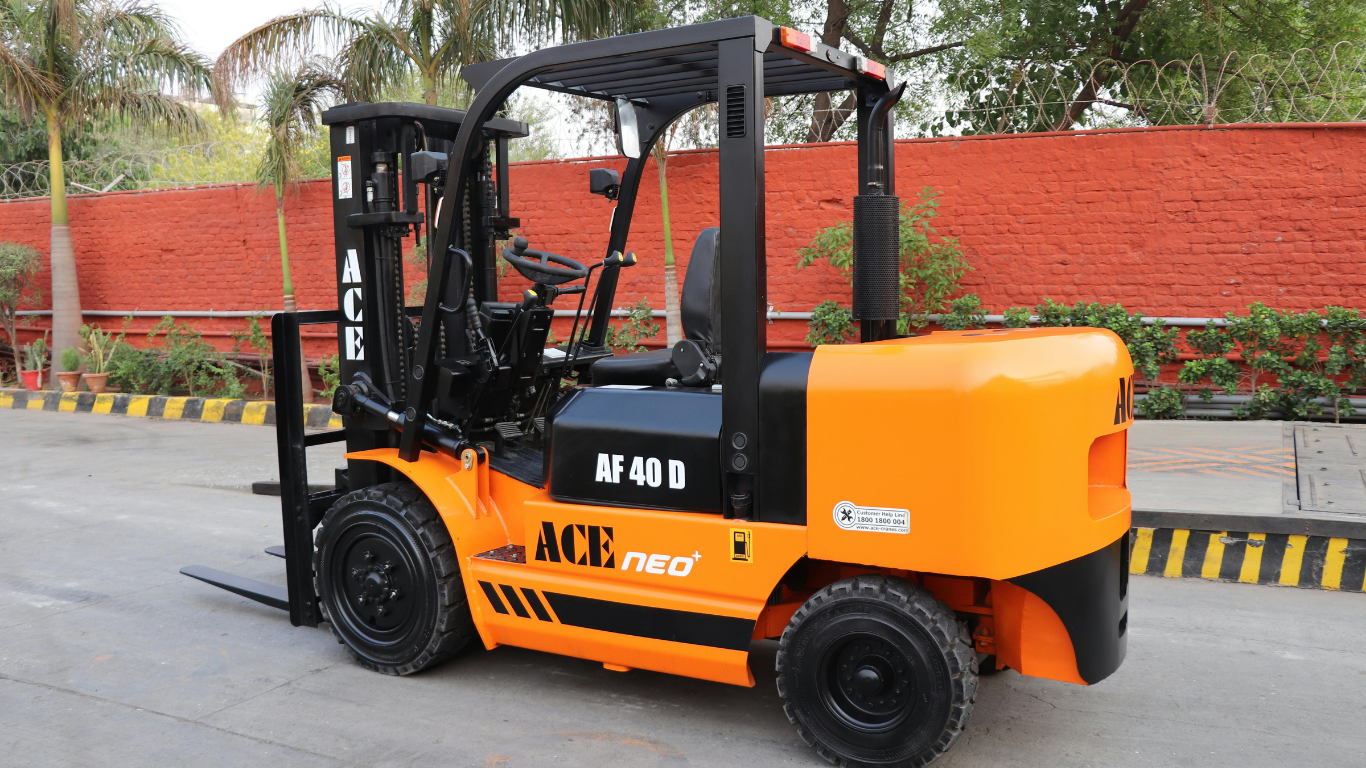 Orange forklift parked outdoors on a wet road beside a red wall and greenery