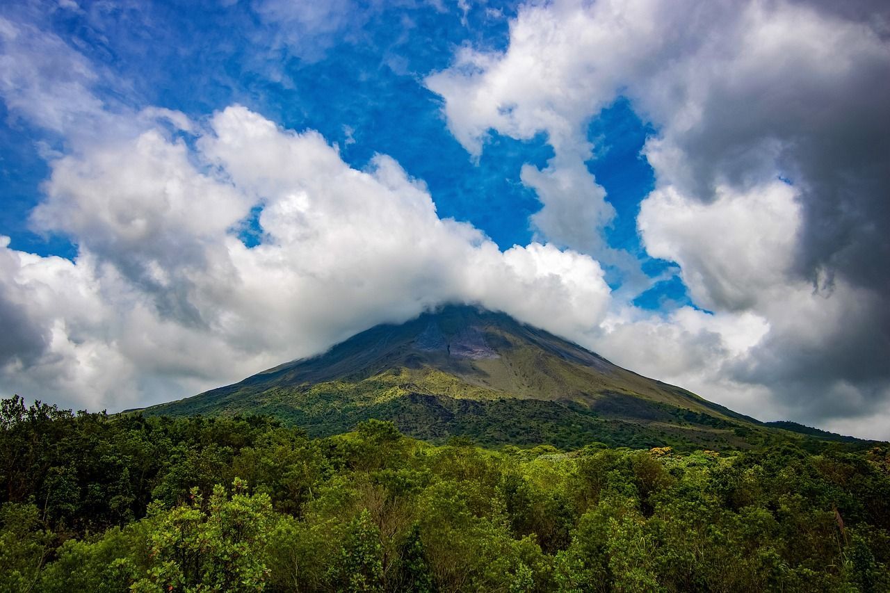 A mountain covered in trees and clouds with a blue sky in the background.