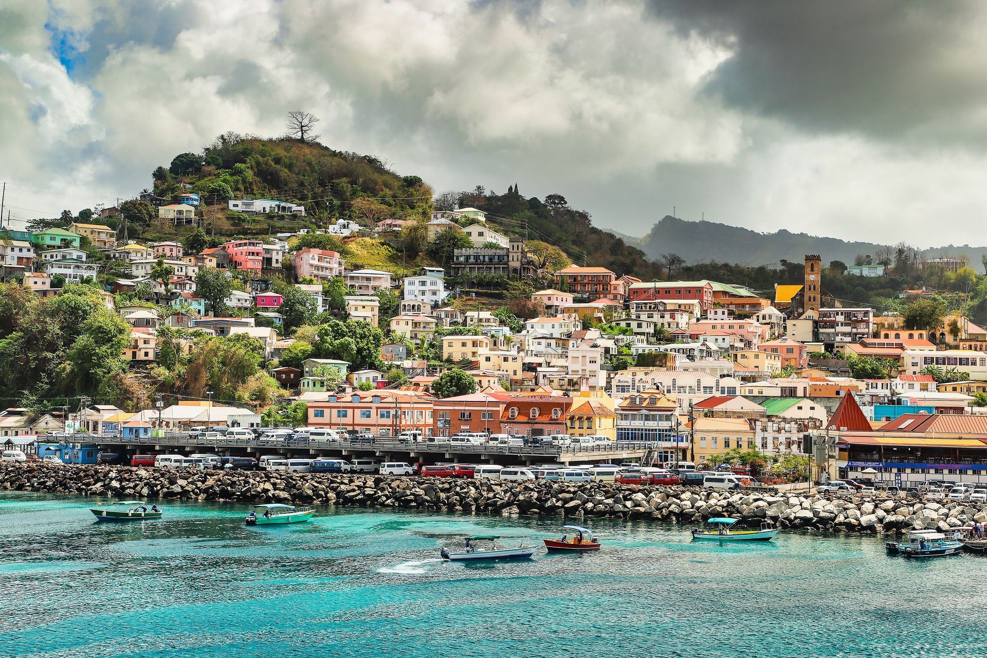 Coastal cityscape of St. George's, Grenada with colourful buildings on a hillside overlooking a turquoise harbour with boats.