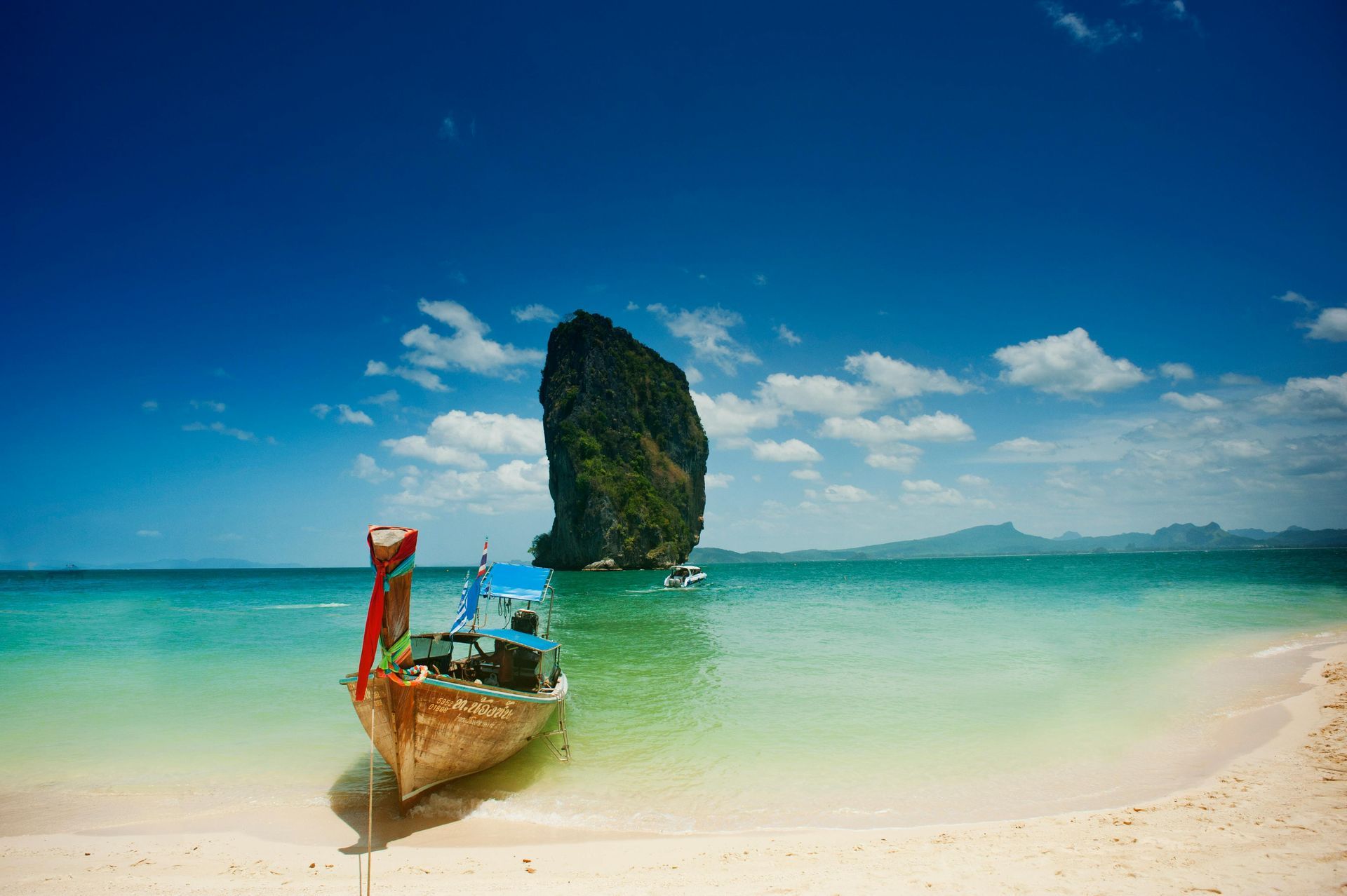 A boat is sitting on a sandy beach next to the ocean in Thailand