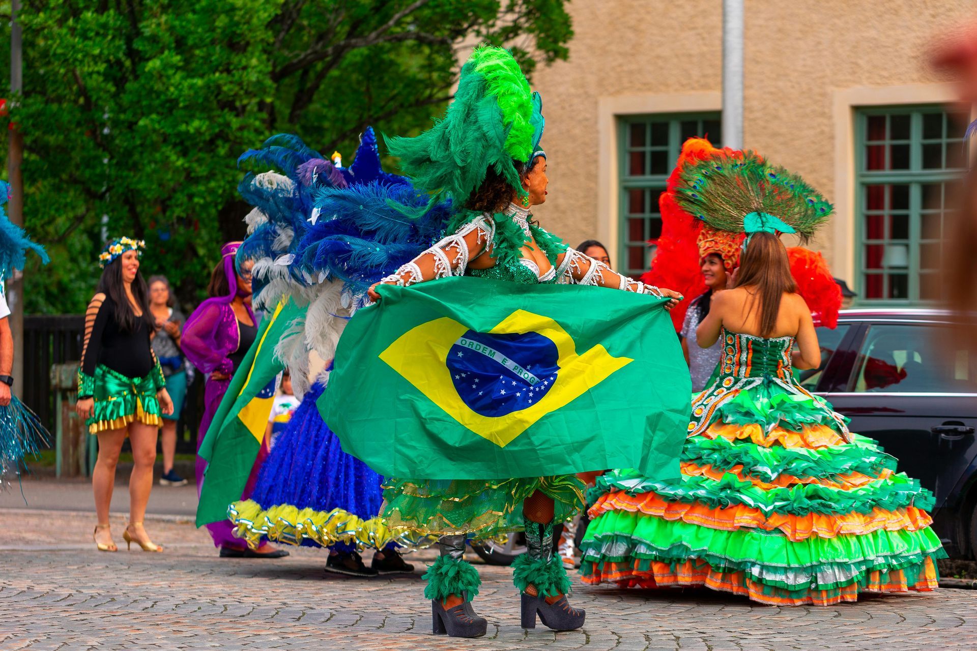 People in colorful Brazilian carnival costumes with the Brazilian flag in a street setting.