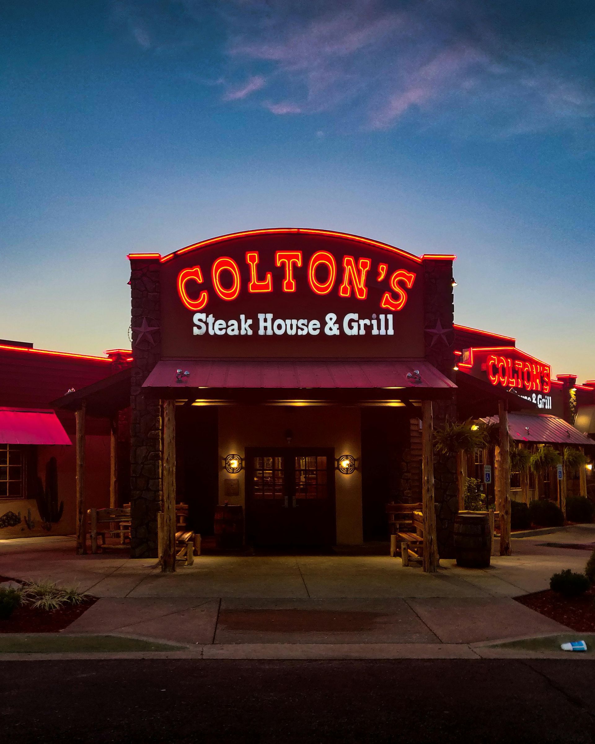 Colton's Steak House & Grill at dusk. The restaurant's red neon sign is lit, with a brick facade and wooden accents.
