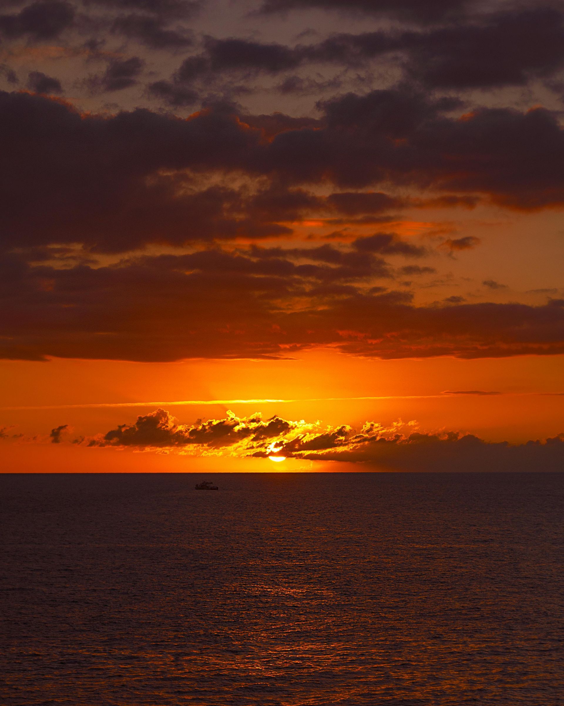 Sunset over ocean with fiery orange and red sky, clouds, and reflecting water.