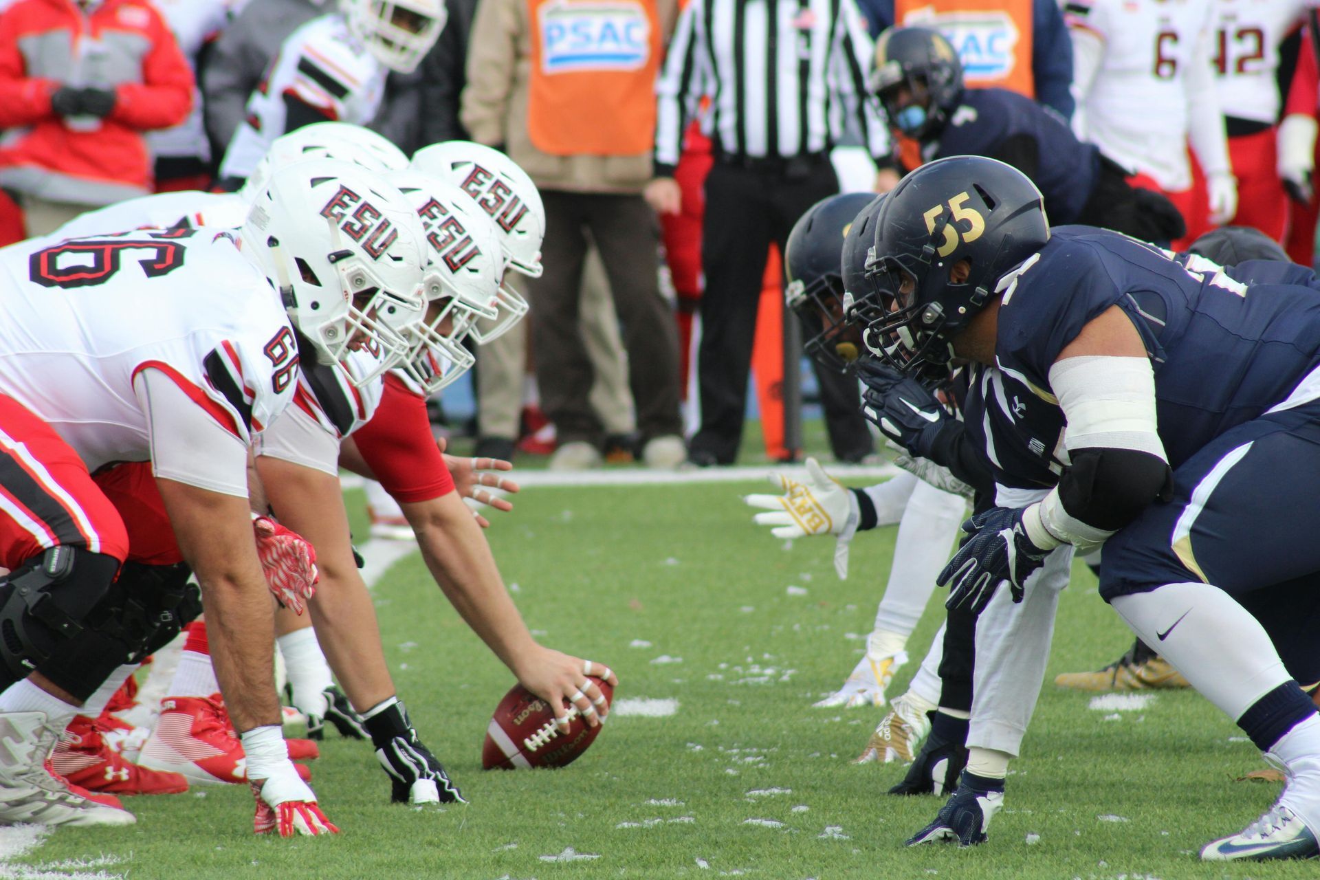 Football players in a line facing each other on a green field, ready to snap the ball.