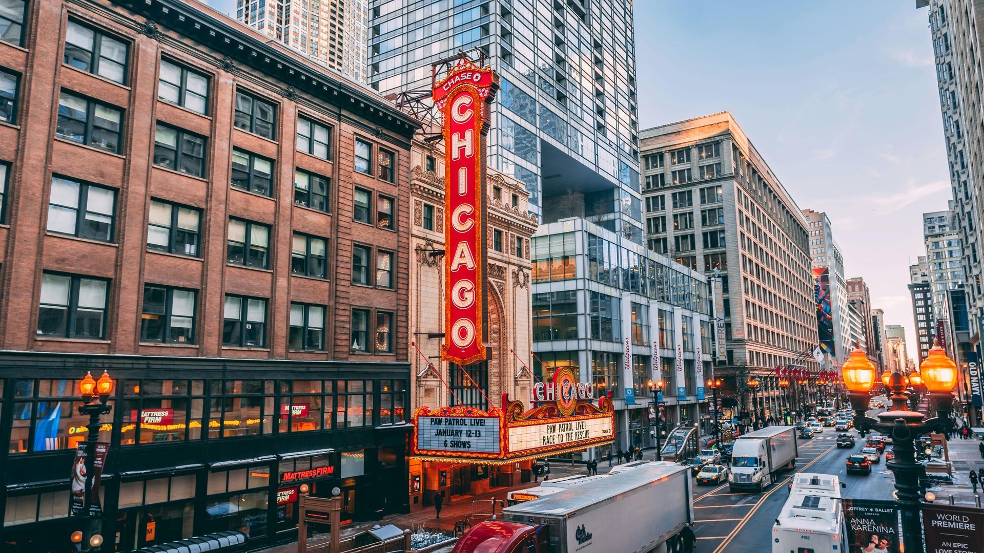 A bustling Chicago street scene with the iconic Chicago Theatre marquee. Traffic moves past tall buildings.