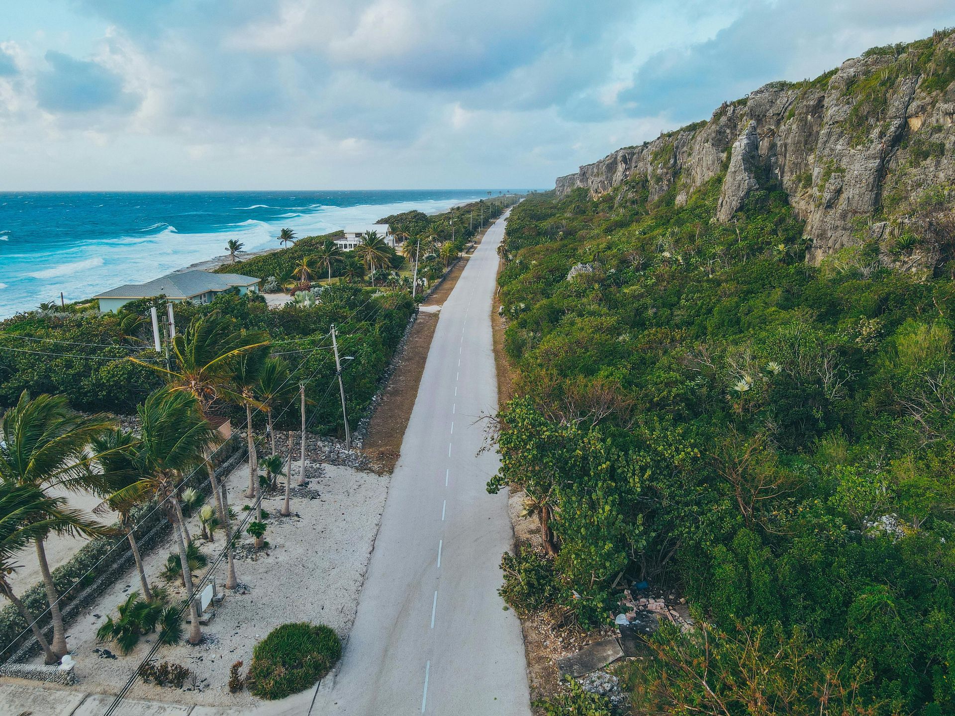 Road along the coast with the ocean on one side and a rocky cliff covered in green vegetation on the other.