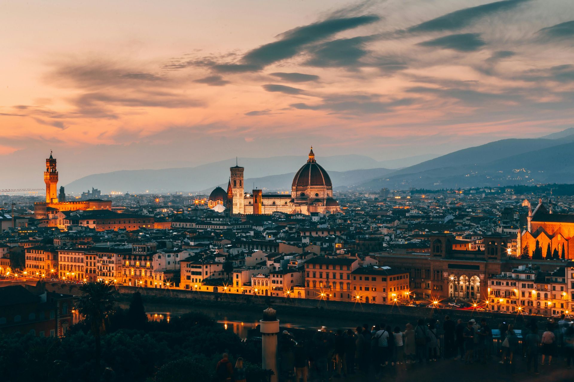 An aerial view of Florence city at night with a sunset in the background.