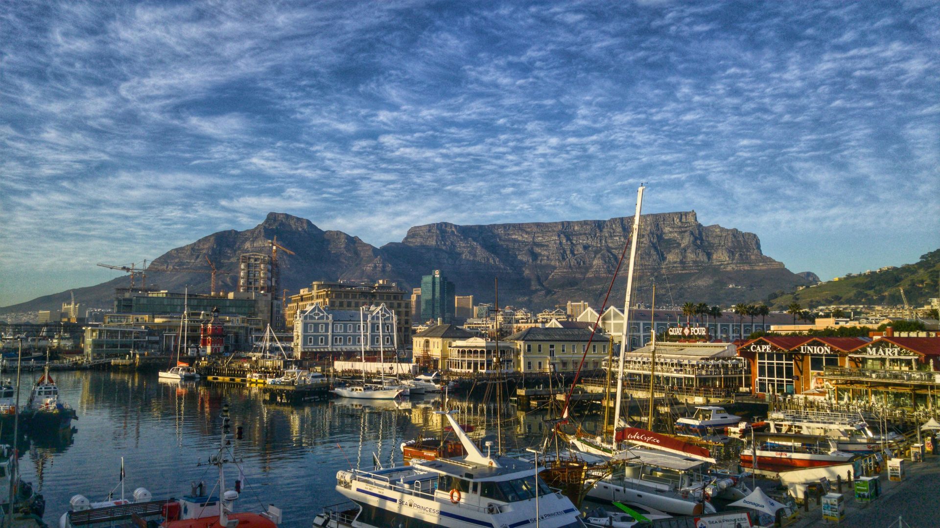 A group of boats are docked in Cape Town harbour with Table mountain in the background.