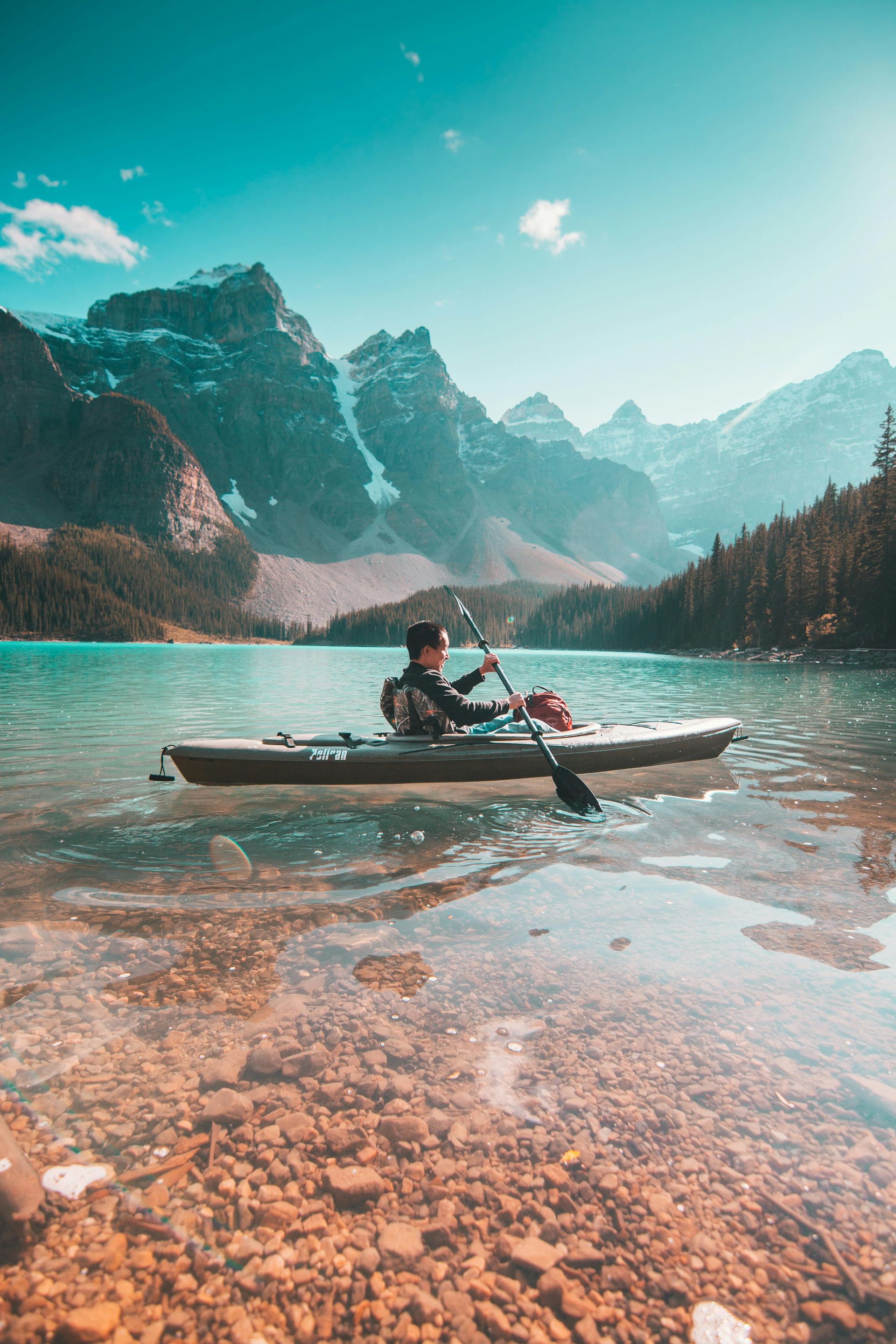 Person kayaking on a turquoise lake with a mountain backdrop under a clear blue sky.
