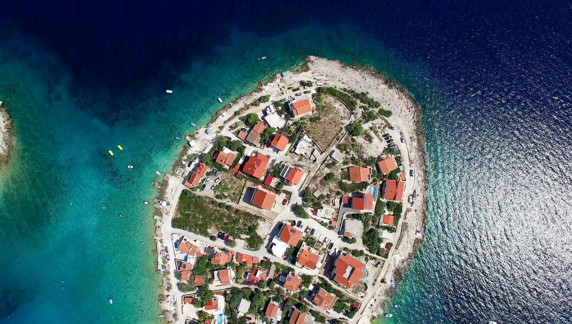 Aerial view of a small island with houses and red roofs surrounded by blue and turquoise water.