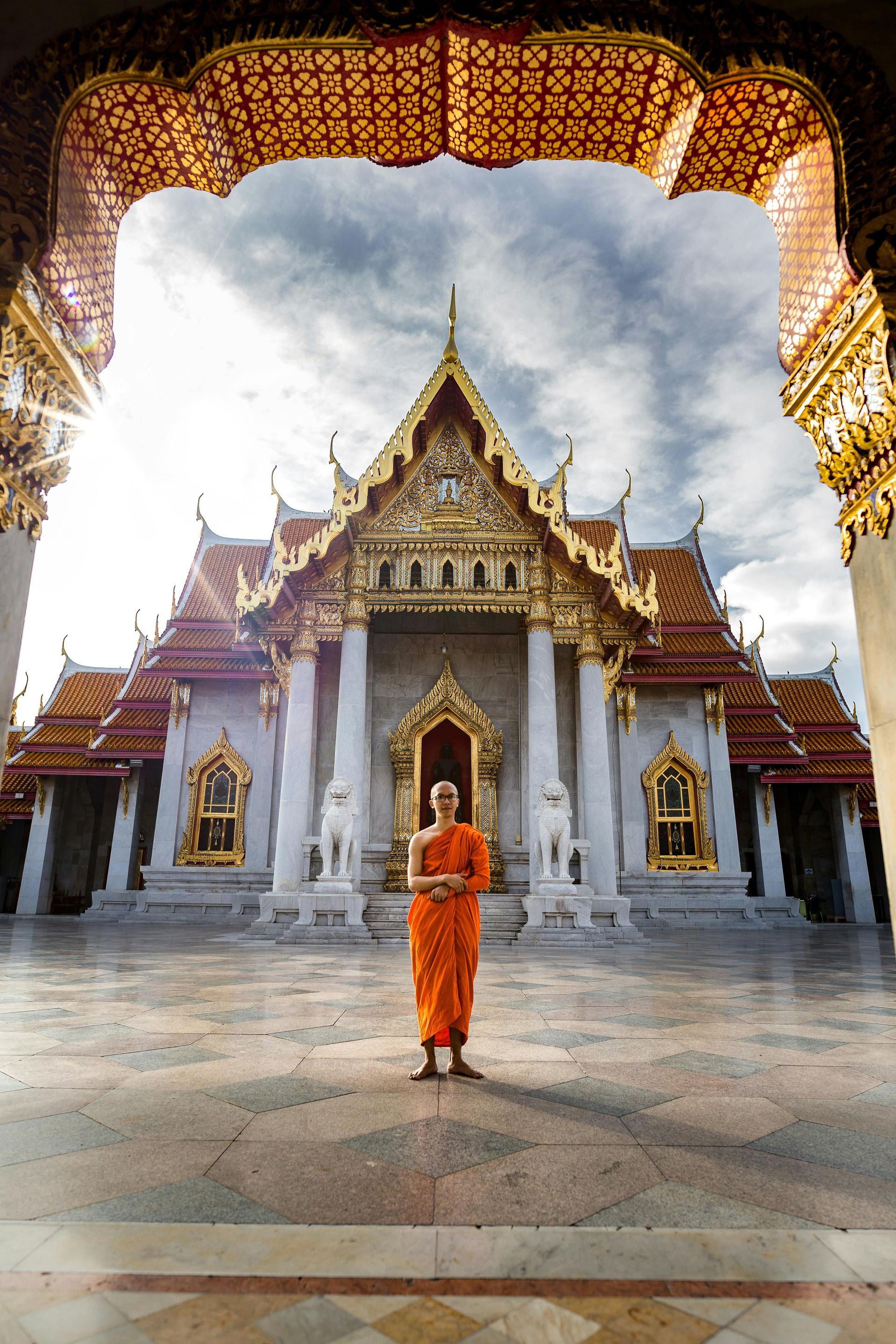 A monk in an orange robe is standing in front of a temple.