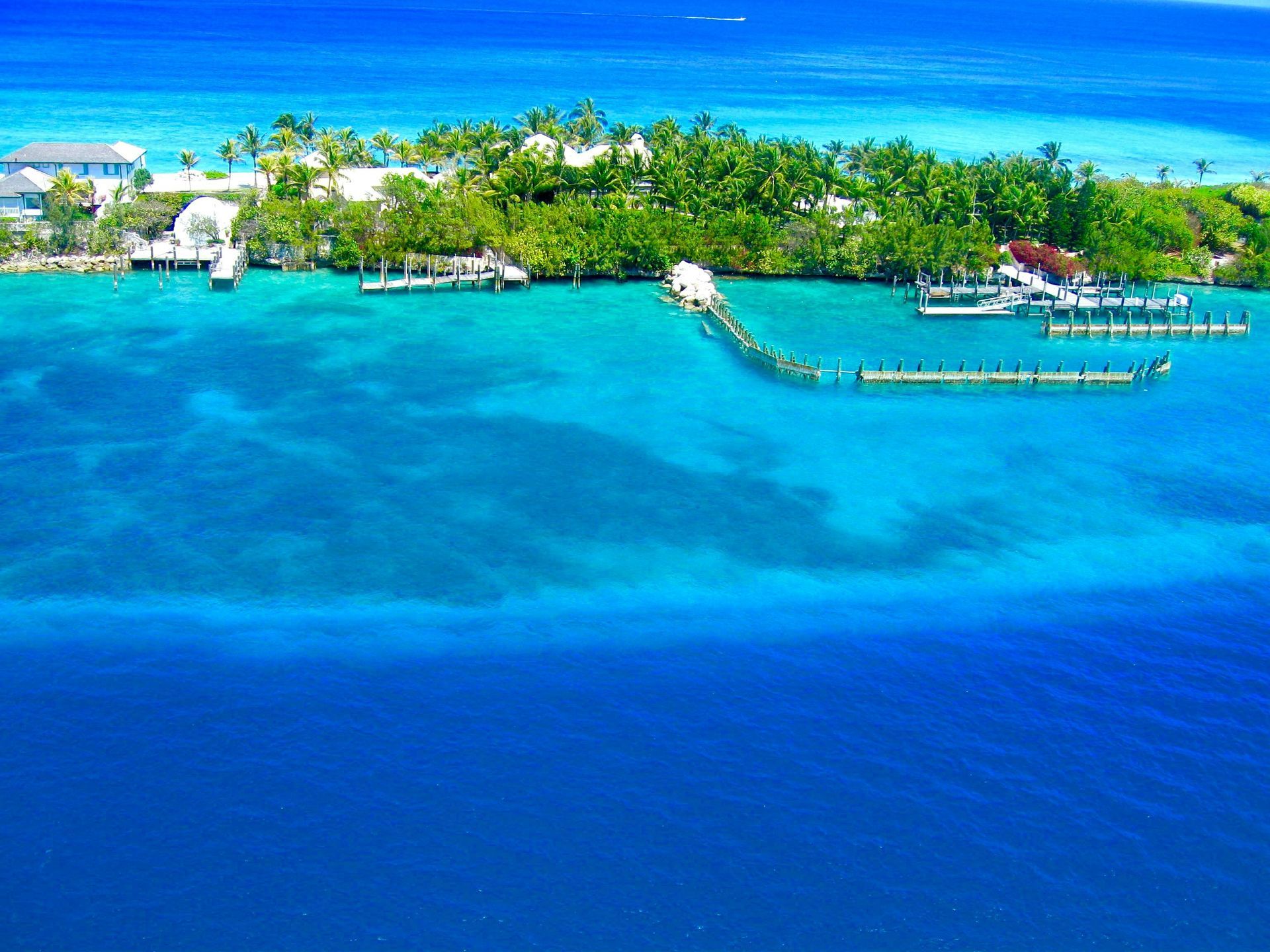 An aerial view shows a lush green island surrounded by turquoise and deep blue water, with docks and buildings visible.