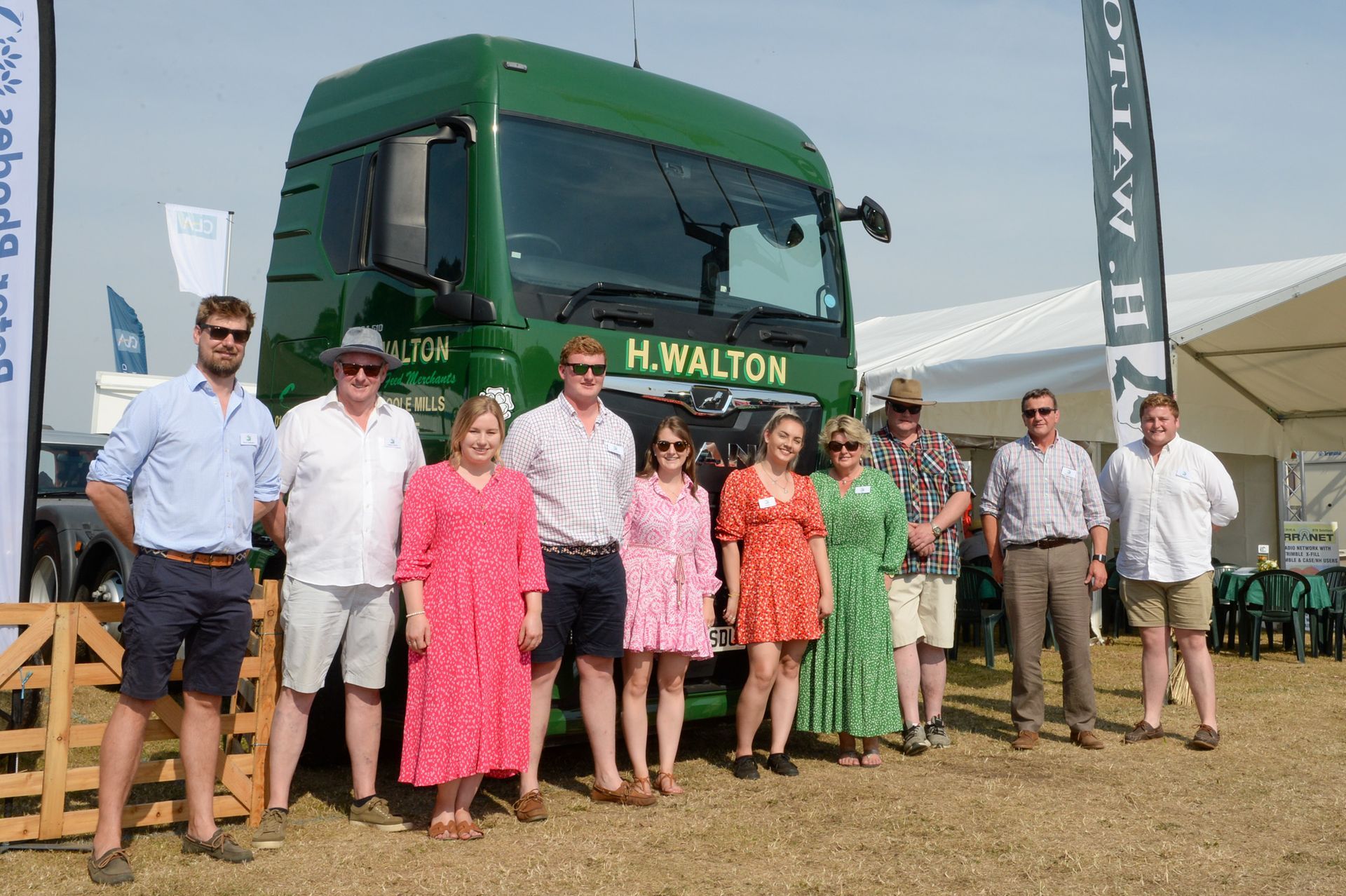 Group posing in front of a green H. Walton truck at an outdoor event