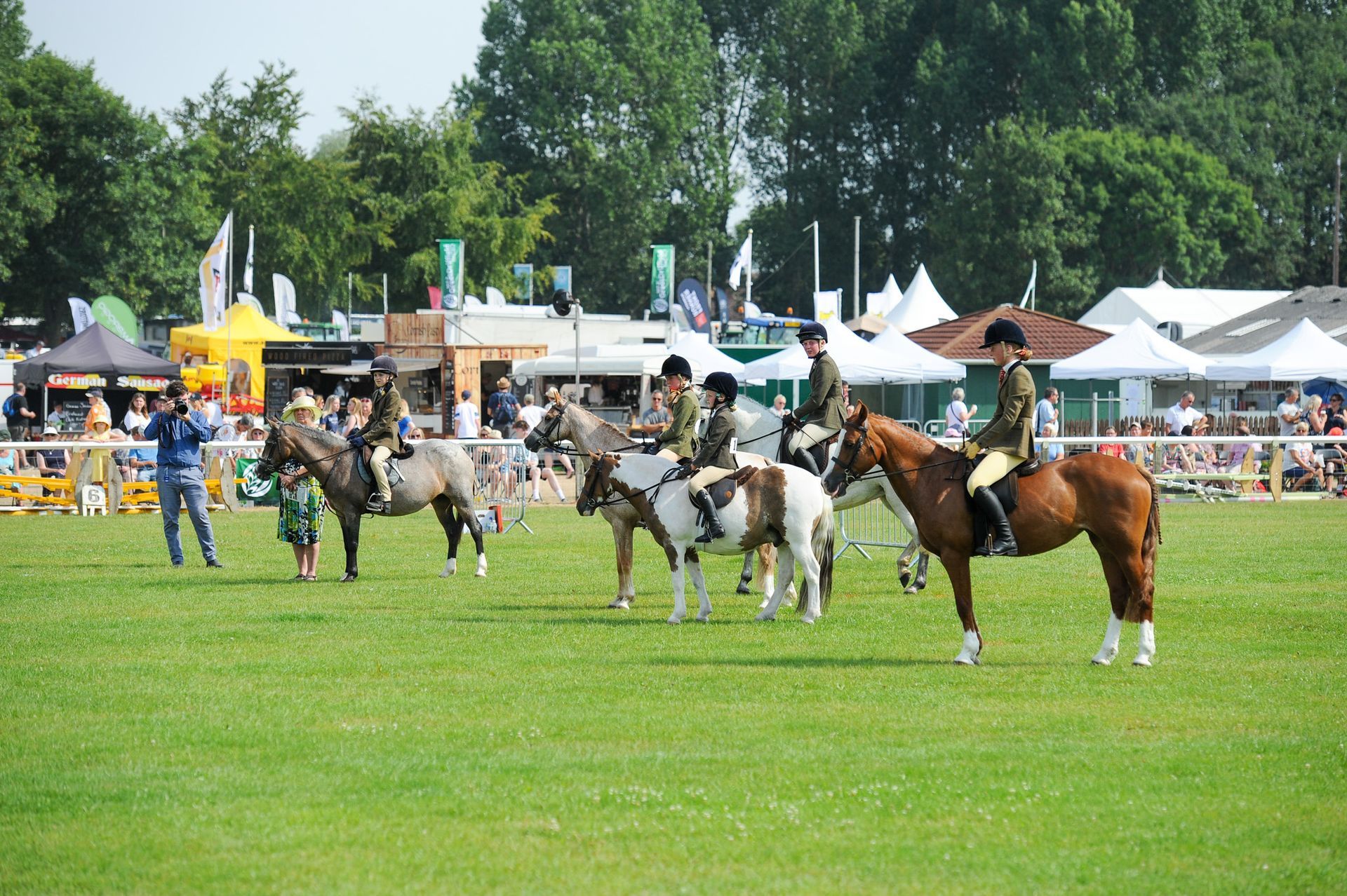 Horse show ring with several riders on decorated horses in a grassy field near tents and spectators