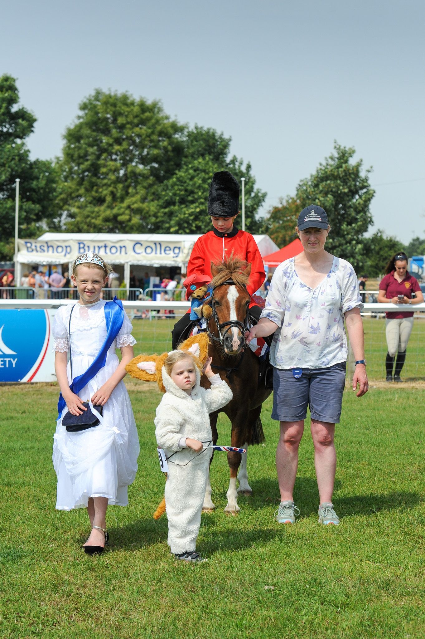 People standing with a horse at a grassy outdoor event near a race track finish line.