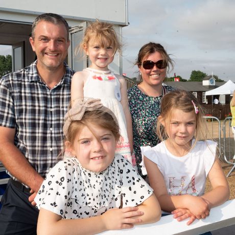 Family of five posing outdoors at an event, with two children in front and two adults behind.