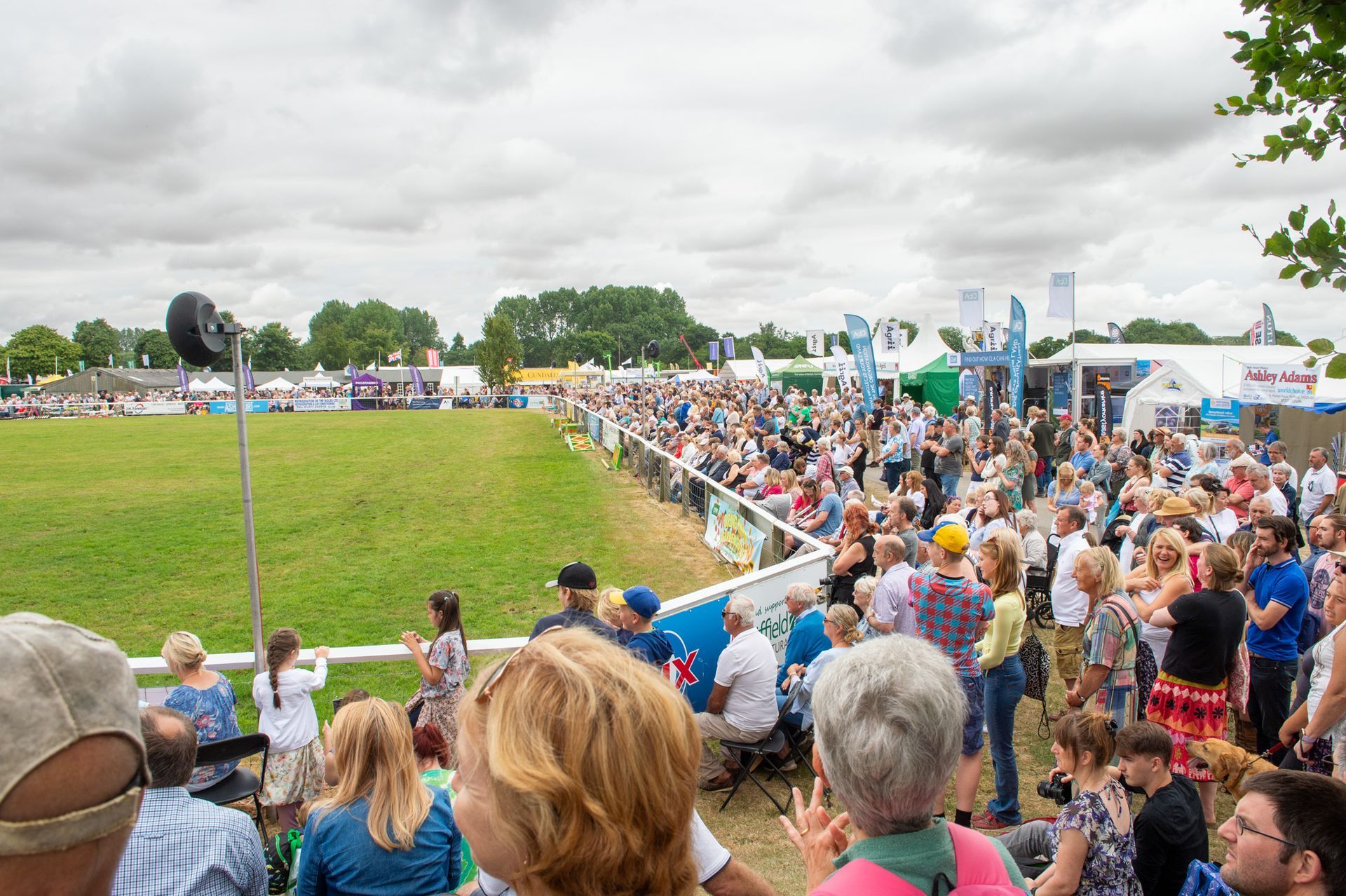 Crowd watching an outdoor sports event beside a grassy field under cloudy skies