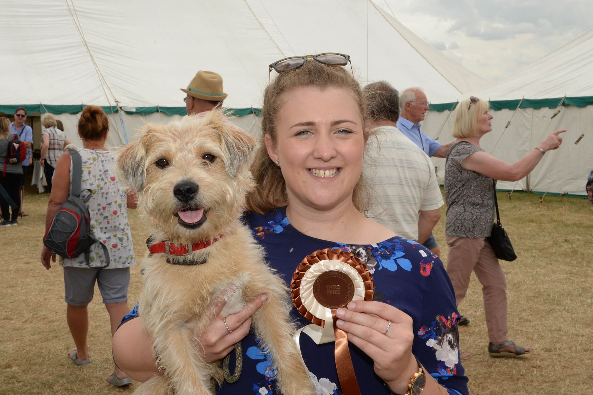 Woman holding a small dog and a ribbon at an outdoor event under a tent