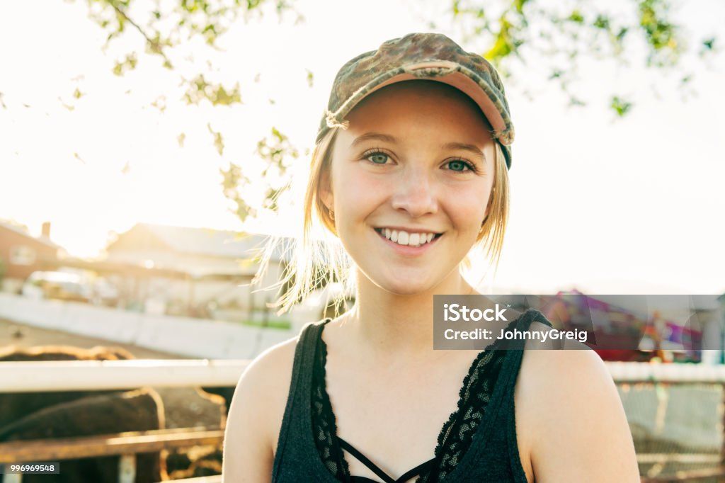 Smiling woman in a cap outdoors at sunset, with warm backlighting and a blurred railing behind her