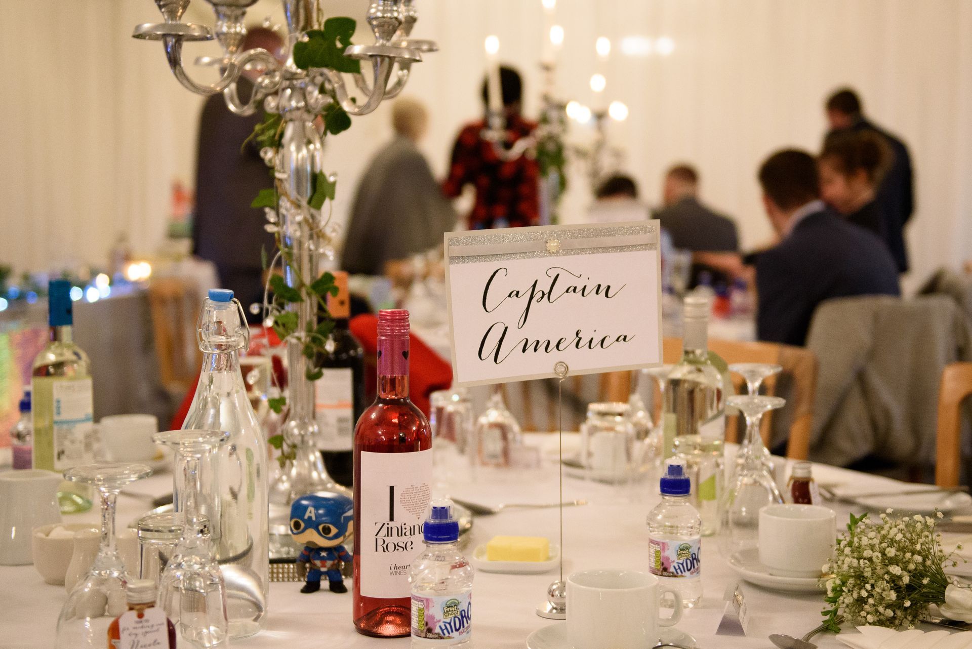 Wedding reception table with wine, glasses, flowers, and a “Congratulations” sign, guests blurred in the background