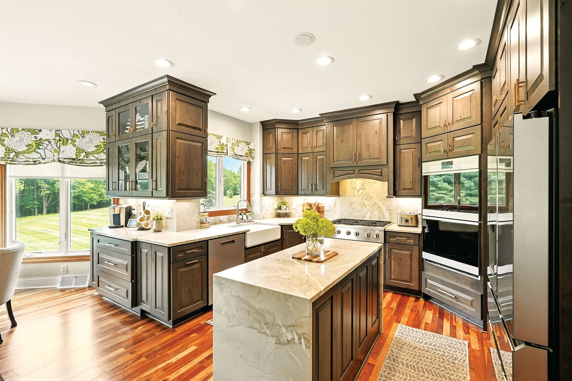 Modern kitchen with dark wood cabinets, a large marble island, stainless steel appliances, and wood floors.