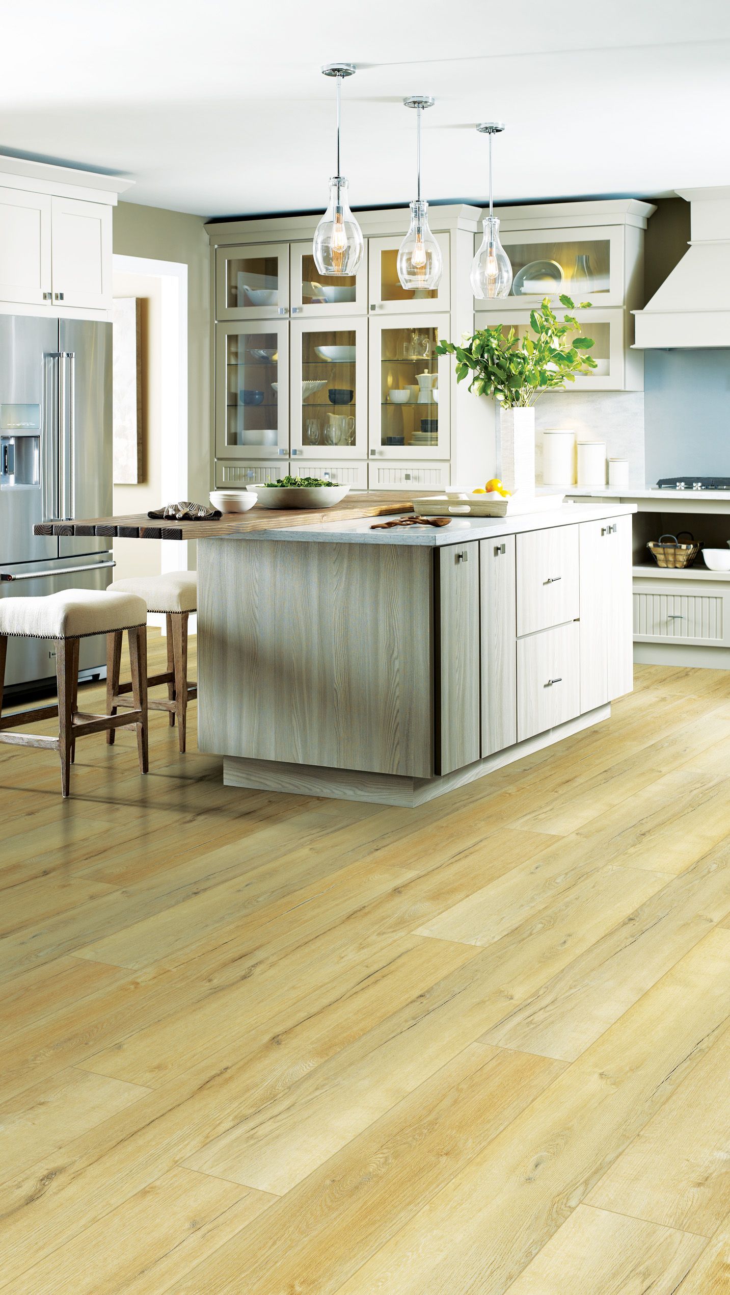 A bright, modern kitchen with white cabinetry, a large central island, light wood floors, and hanging pendant lights.