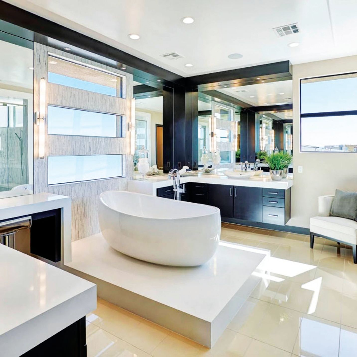 A modern master bathroom featuring a white freestanding tub on a platform, a dark vanity, and large glass windows.
