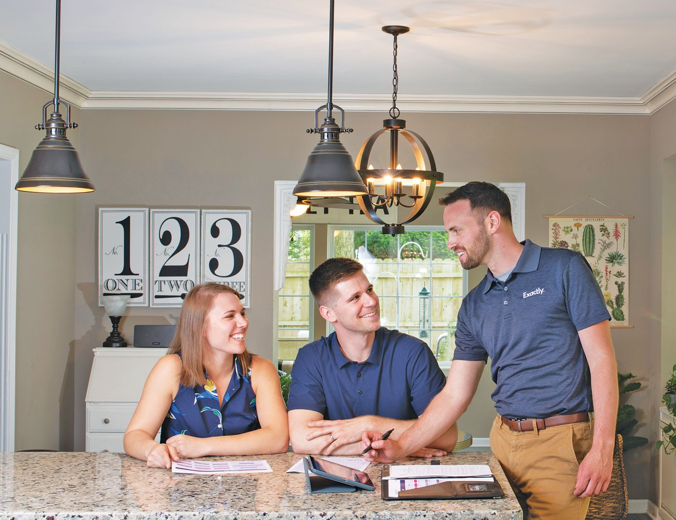 A professional in a branded polo shirt consults with two people at a kitchen island, reviewing documents together.