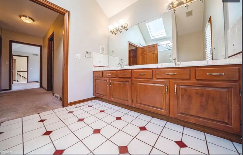 A bathroom with a double wood vanity, large mirror, and white tiled floor featuring a red diamond grid pattern.