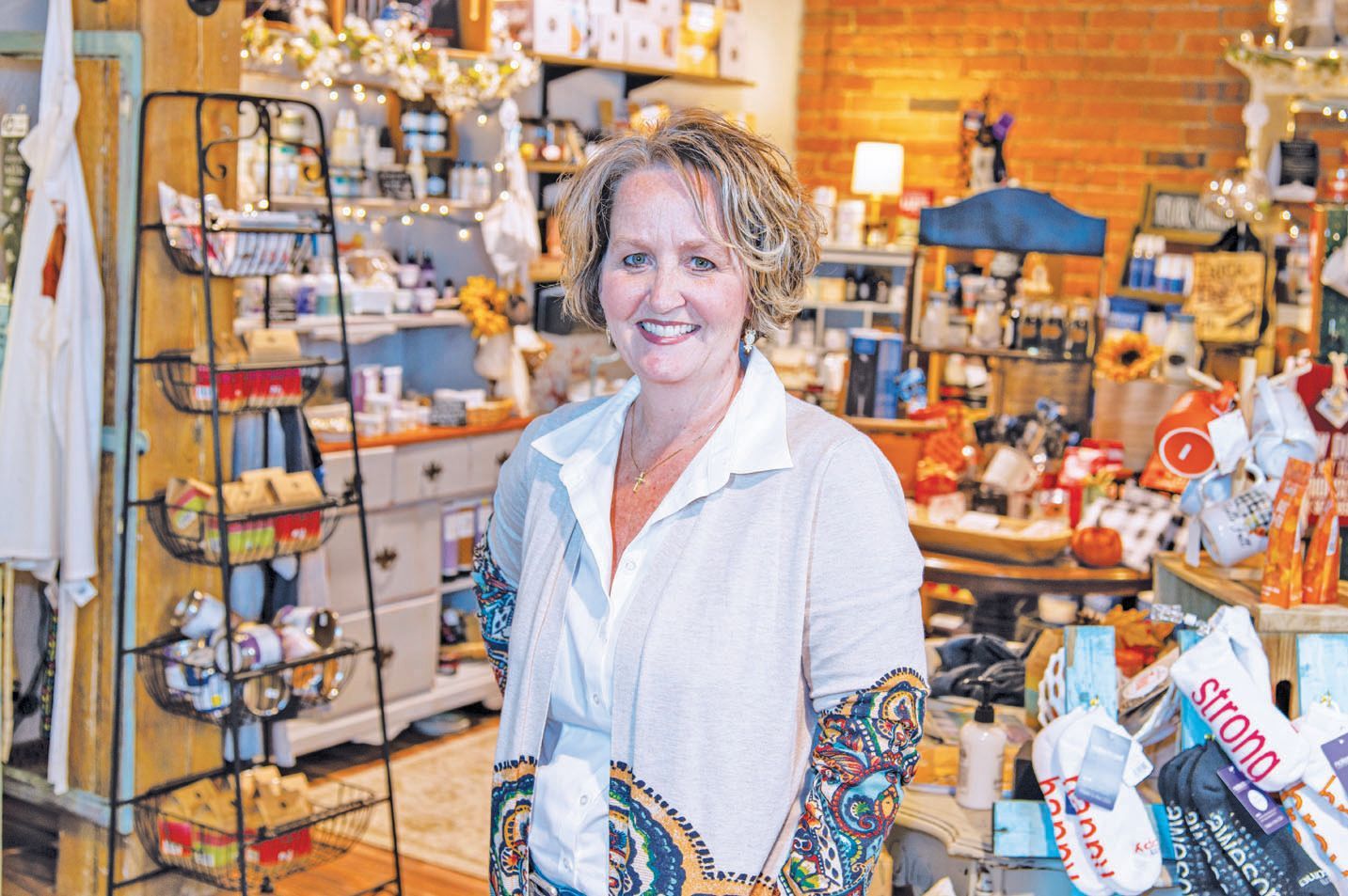 A smiling person stands in a retail store filled with shelves of products and decor.