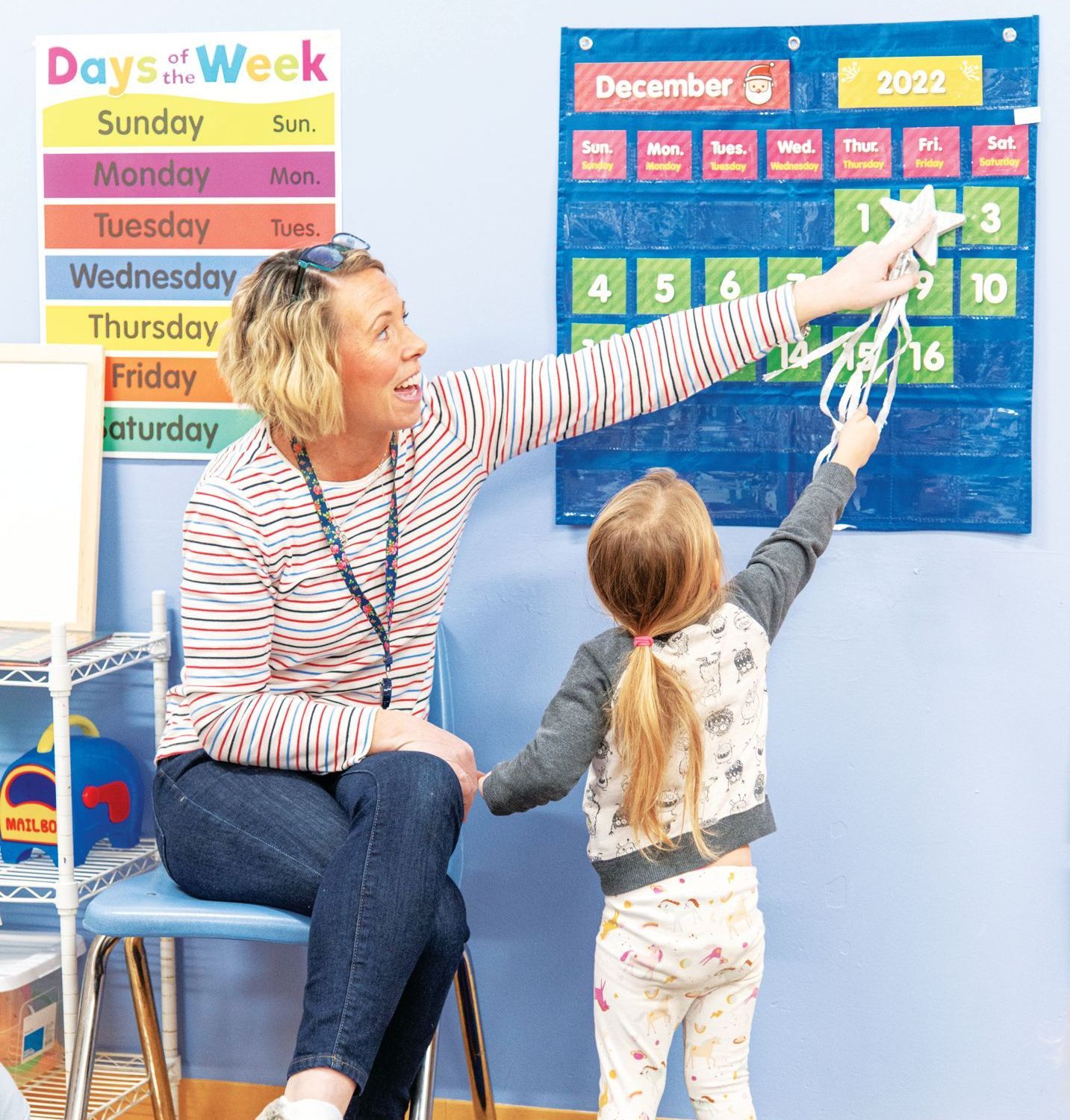 An instructor and child point to the number two on a classroom December 2022 wall calendar.