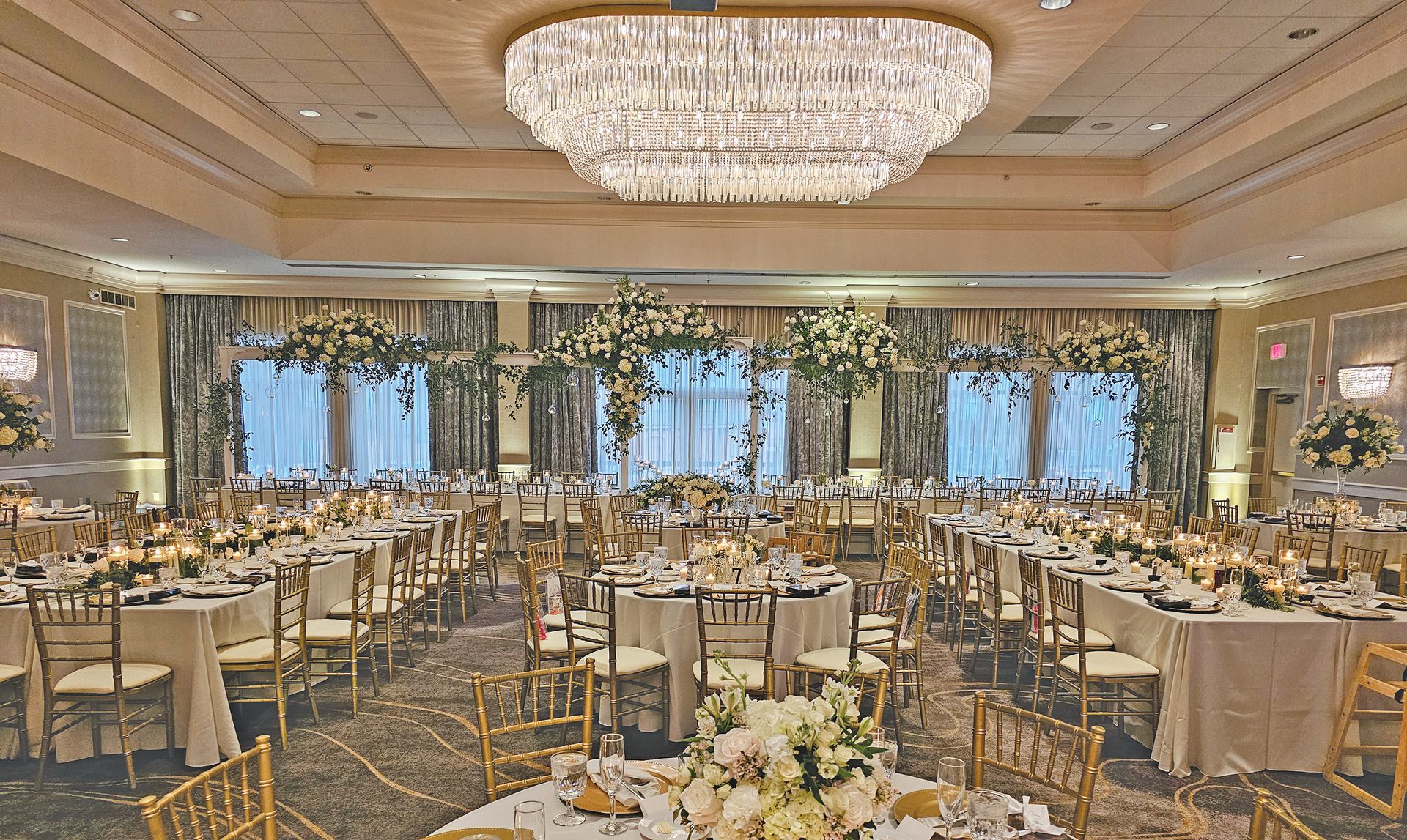 A banquet hall set for a formal event with round and rectangular tables, floral centerpieces, and a large chandelier.