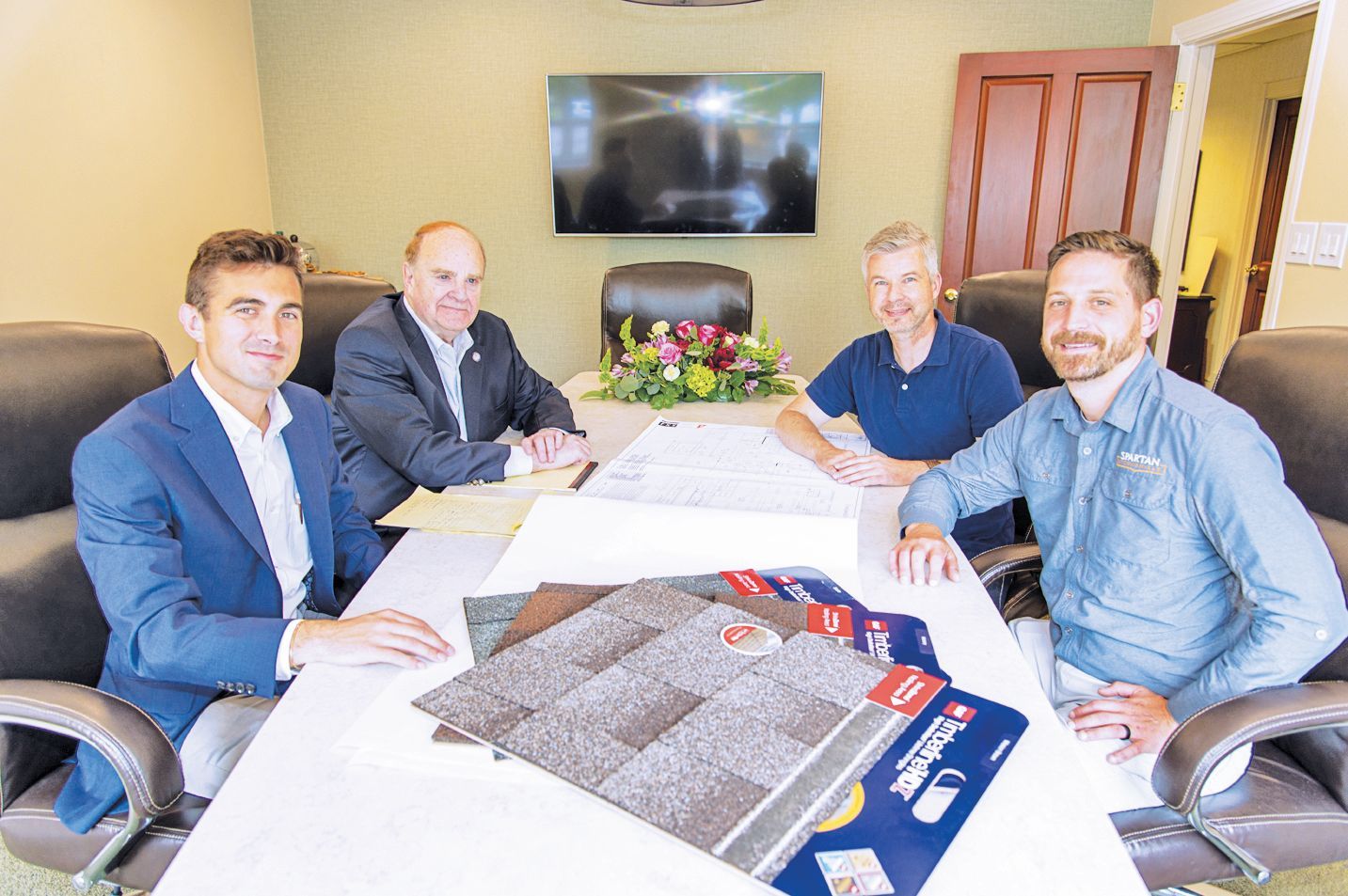 Four men sit around a conference table with building material samples, looking toward the camera in an office.