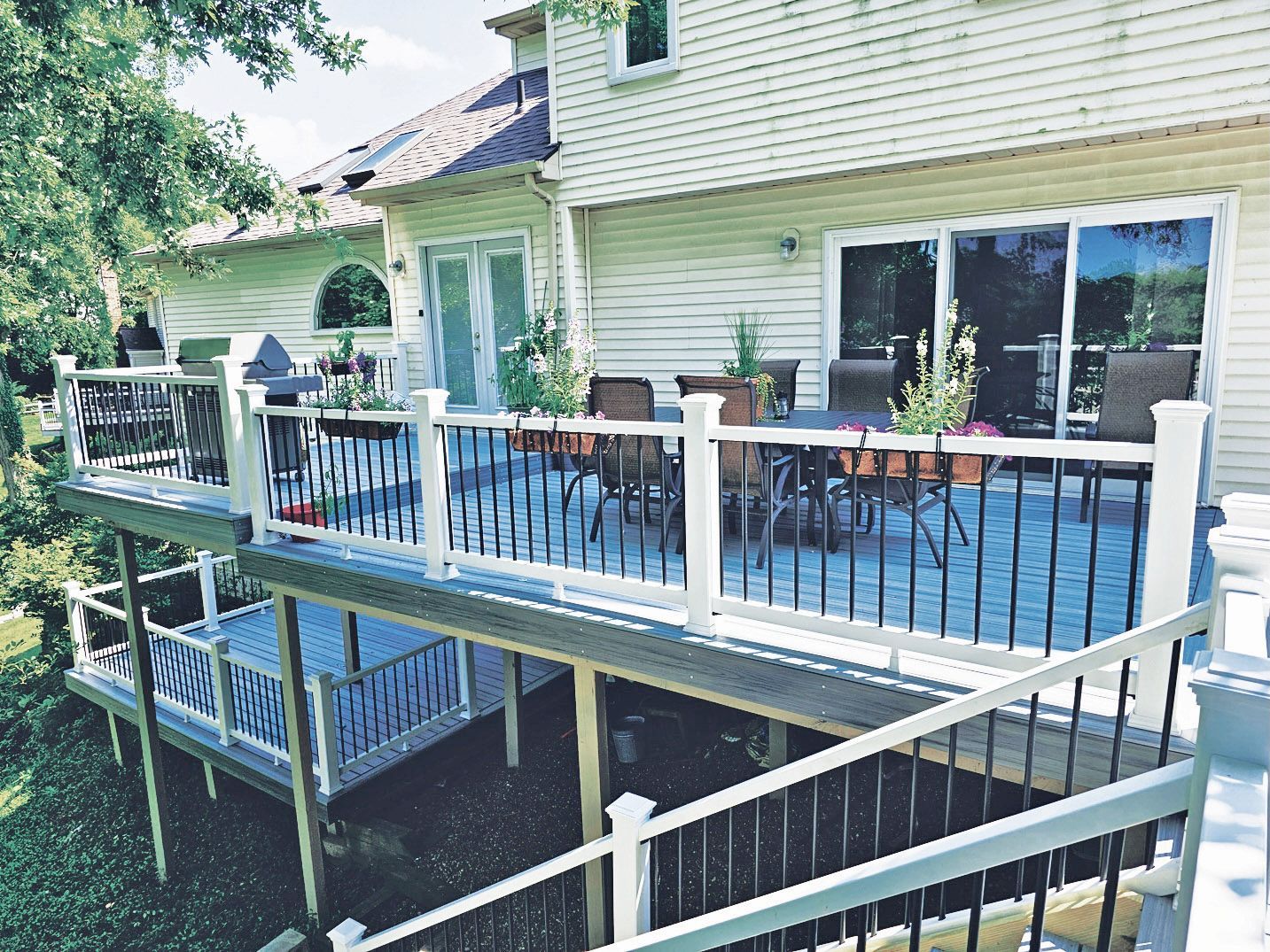 A multi-level backyard deck with white railings and black balusters, featuring outdoor furniture and sliding doors.