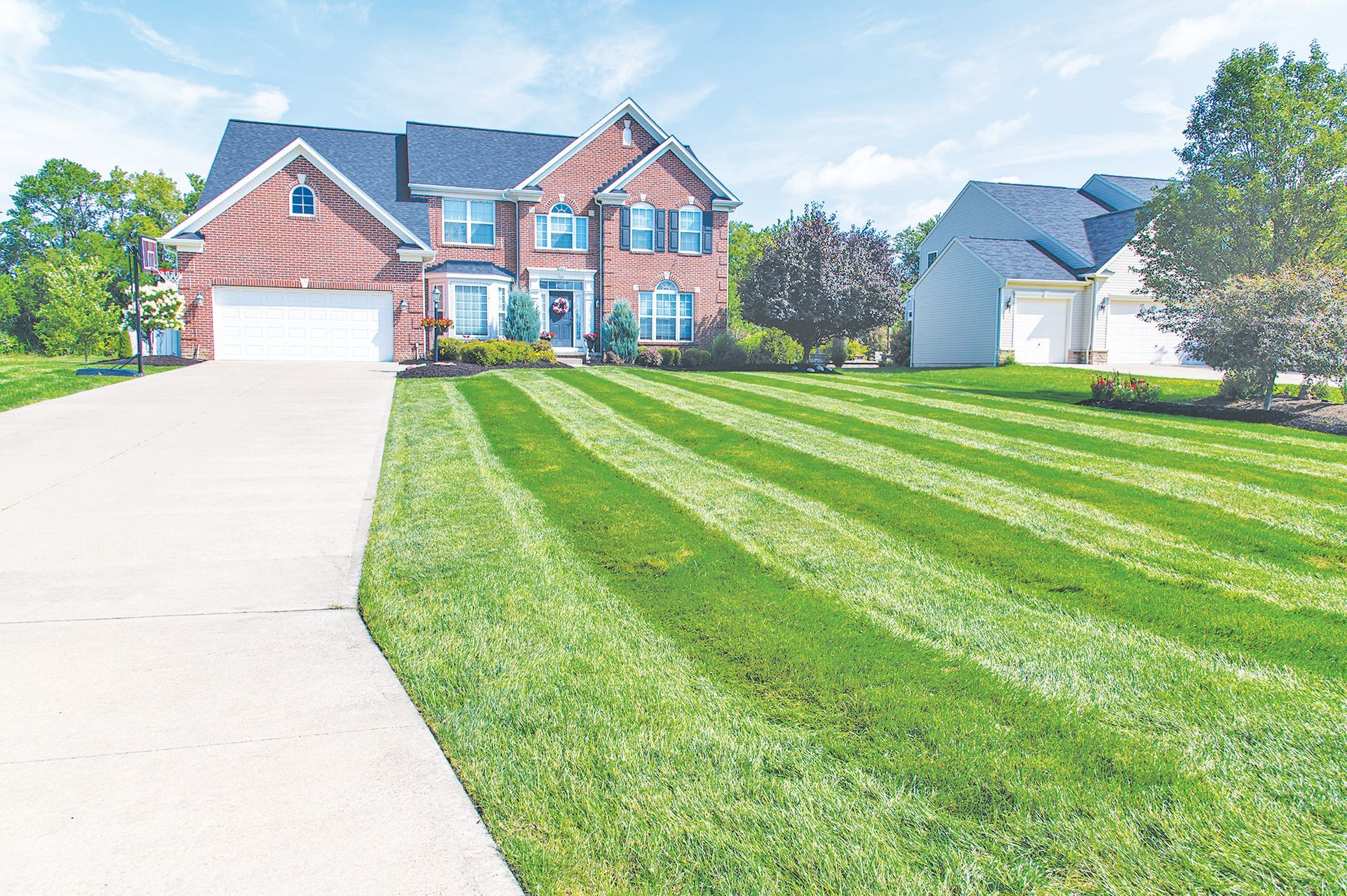 A brick, two-story house with a white garage sits behind a front yard featuring distinct, freshly mowed lawn stripes.