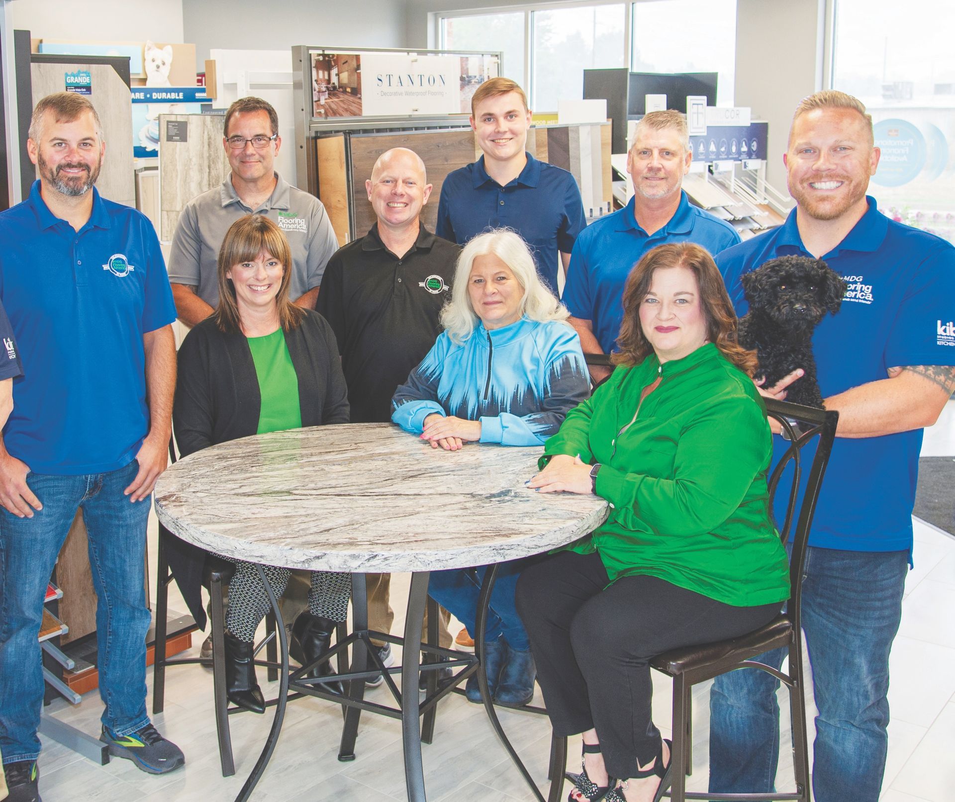 A group of professionals in a showroom standing around a round stone table, some wearing blue polo shirts.