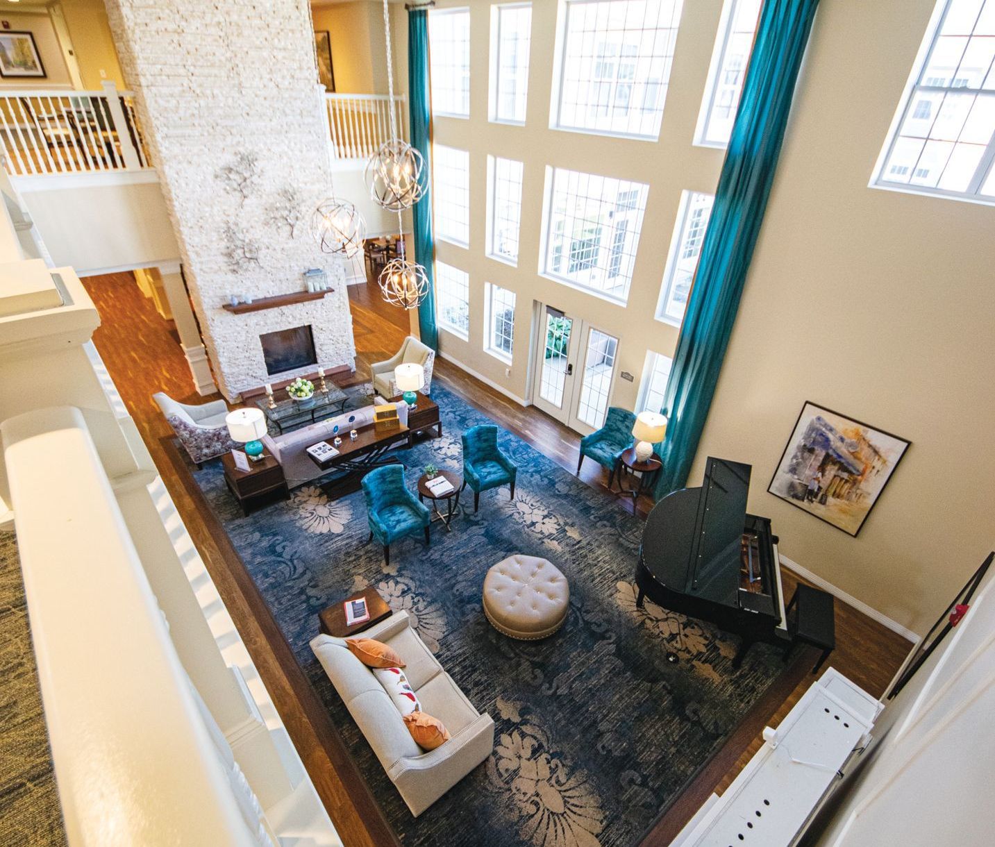 High-angle view of a living room with a large white stone fireplace, blue chairs, a grand piano, and a rug on wood floors.