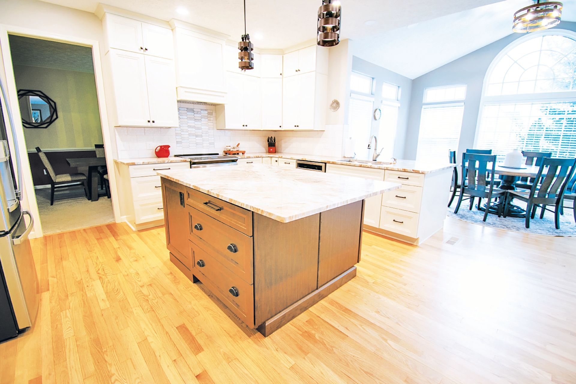 A modern kitchen features white cabinetry, a large wood-toned center island with light countertops, and light wood floors.