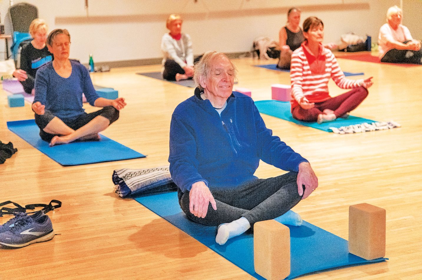 People sit in a meditative pose on yoga mats in a bright studio.