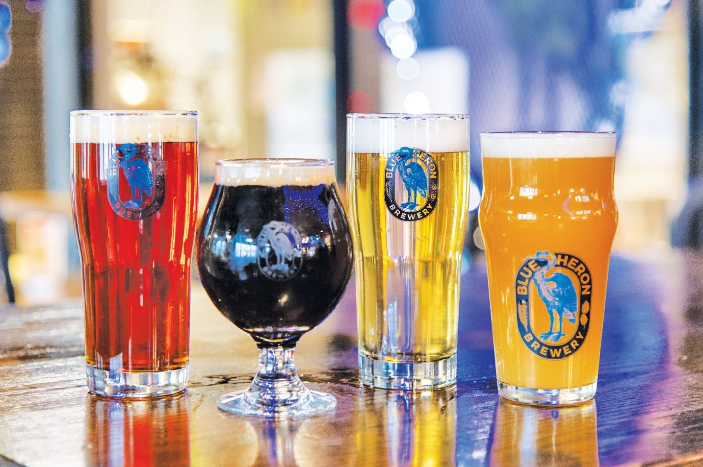 Four glasses of beer of varying colors and styles lined up on a wooden table.
