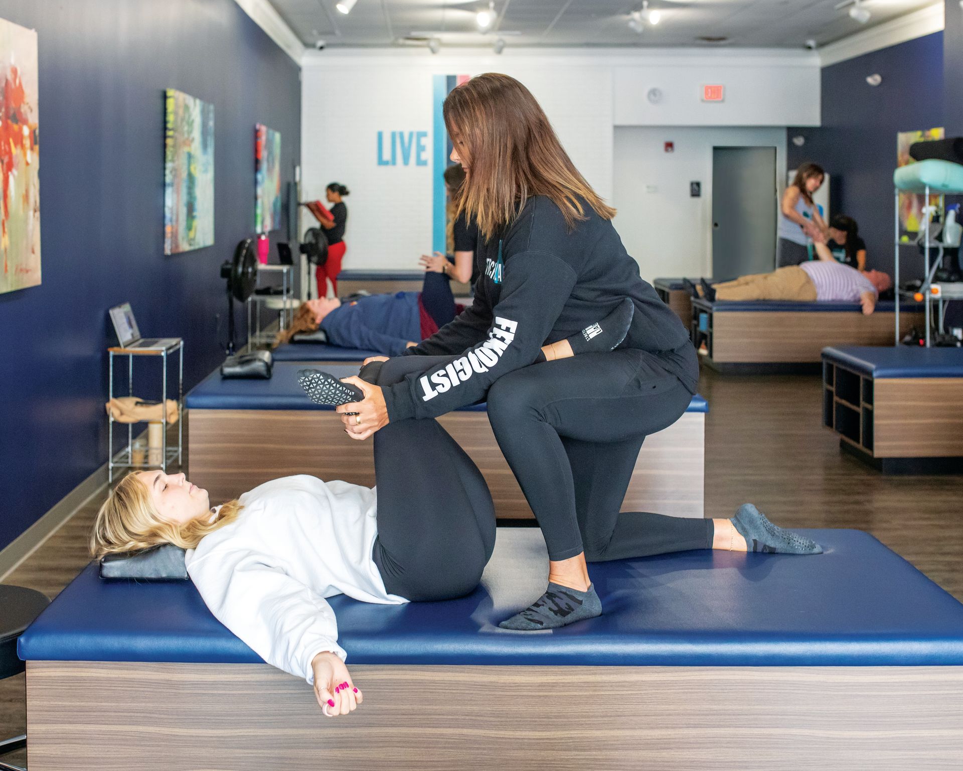 A professional performs a stretching session on a client lying on a treatment table in a fitness studio.