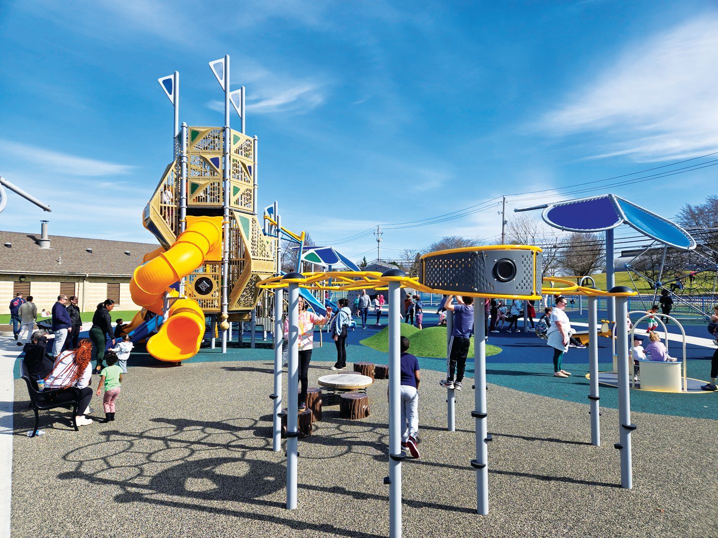 A sunny playground featuring a tall, tan tower with a yellow spiral slide and a yellow overhead monkey bar obstacle course.