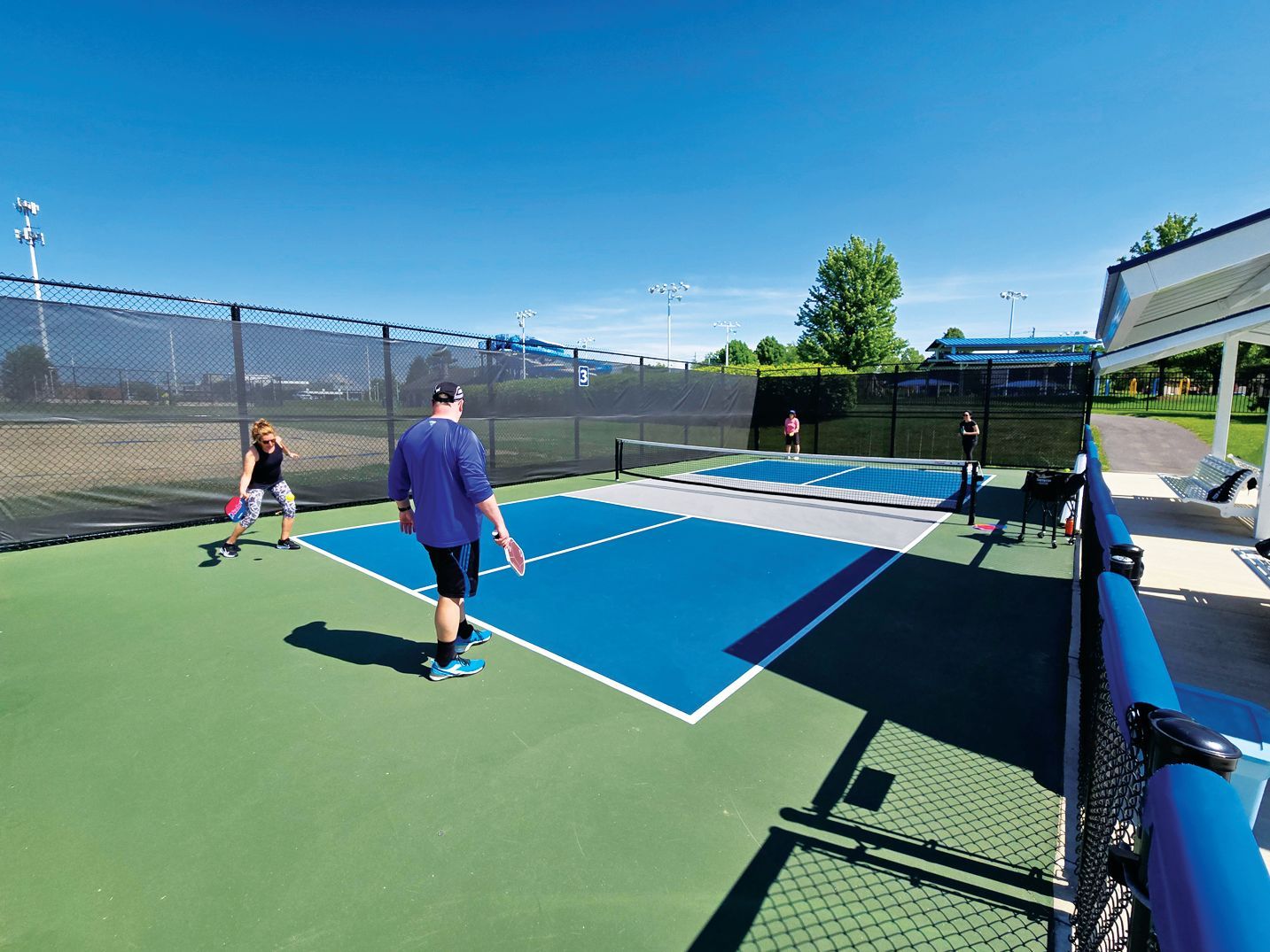 People playing pickleball on an outdoor blue and green court on a sunny day.