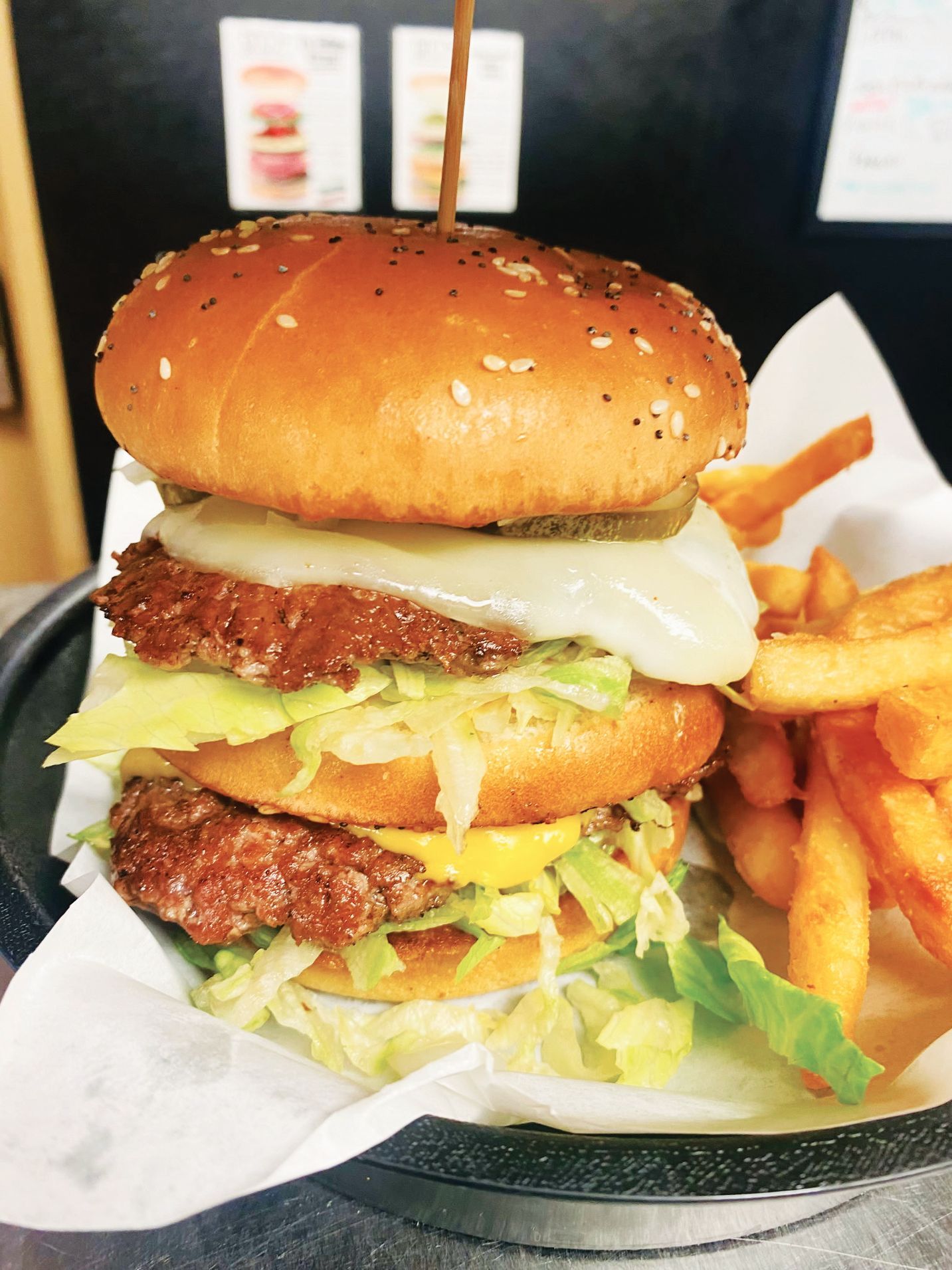 A double-patty burger with cheese, lettuce, and pickles served with a side of golden french fries on a paper-lined tray.