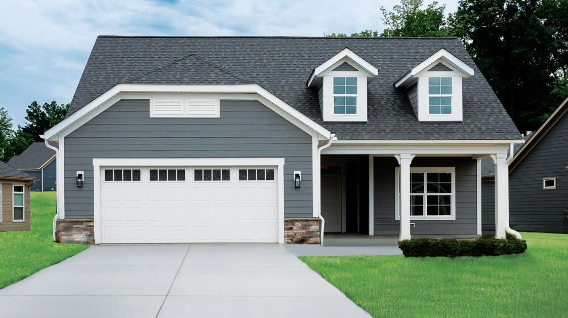A gray two-story house with a white garage door, two front roof dormers, a front porch, and a green lawn.