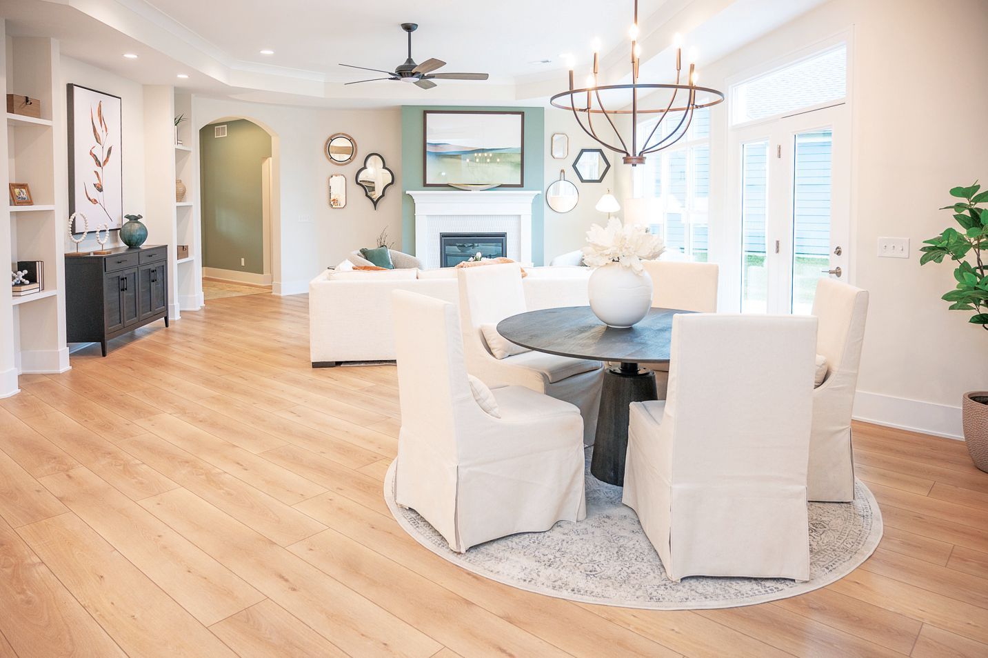 An open-concept living and dining area featuring light wood floors, white slipcovered chairs, and a round dining table.