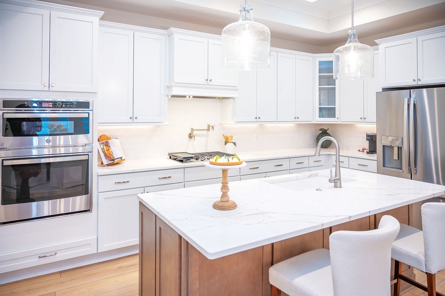 Modern kitchen with white cabinetry, a large marble-topped island with two stools, and stainless steel appliances.