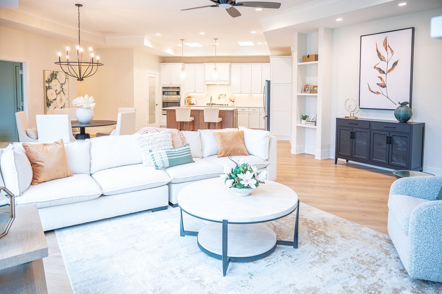 Open-concept living room featuring a white sofa, round coffee table, dining area, and kitchen in a bright, modern home.