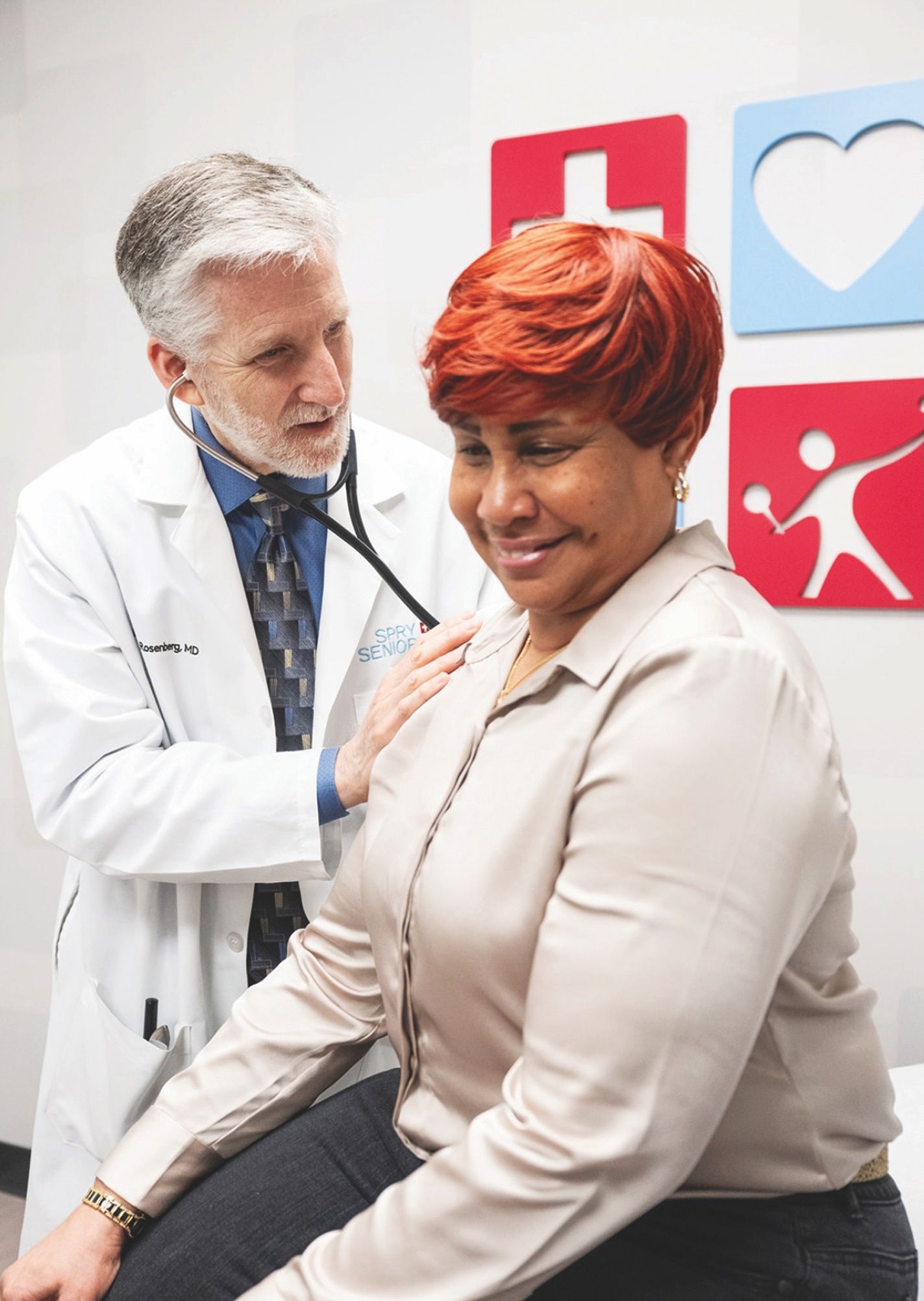 A doctor in a white coat uses a stethoscope to examine a patient sitting in a clinical office.